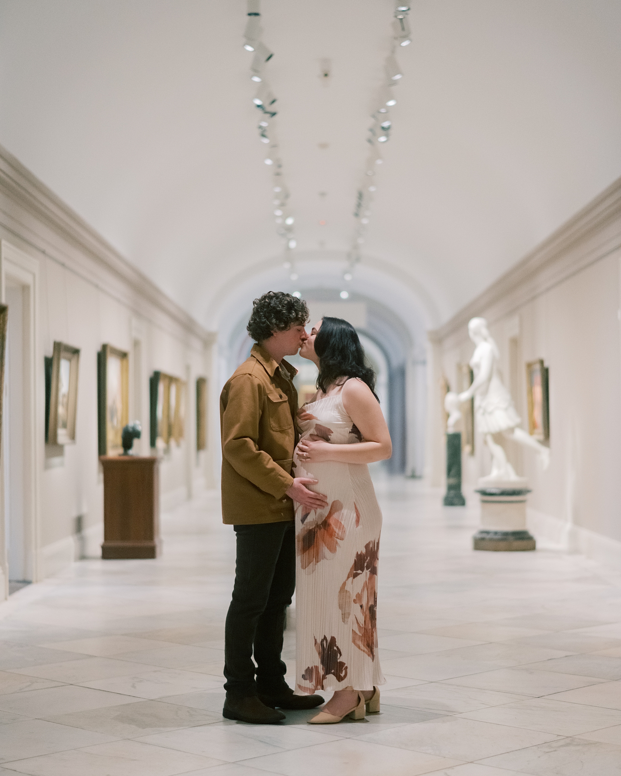 man and woman kiss inside the National Portrait Gallery while woman holds baby bump