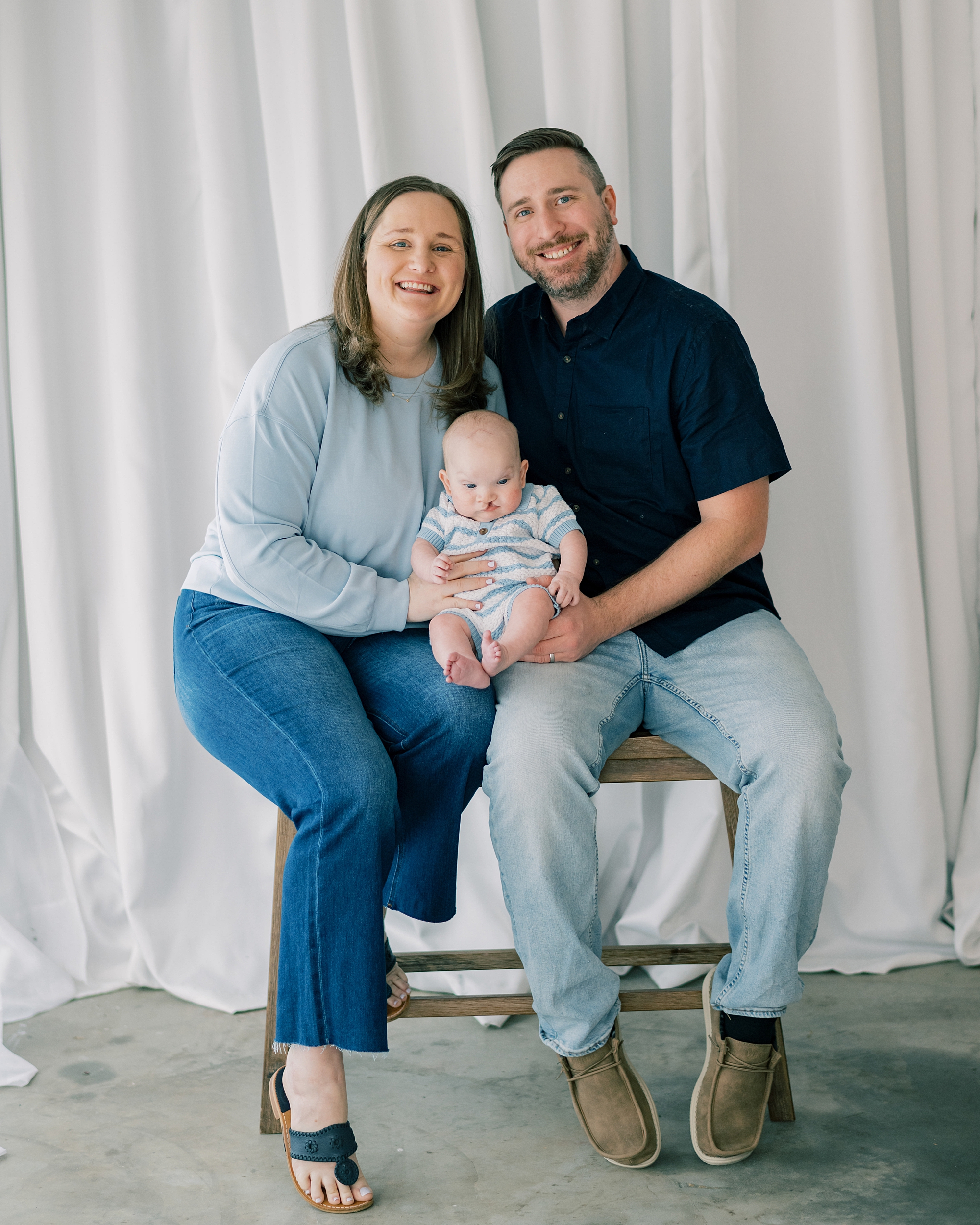 mom and dad sit together with baby with cleft palate on their lap during milestone session in Southern Maryland studio