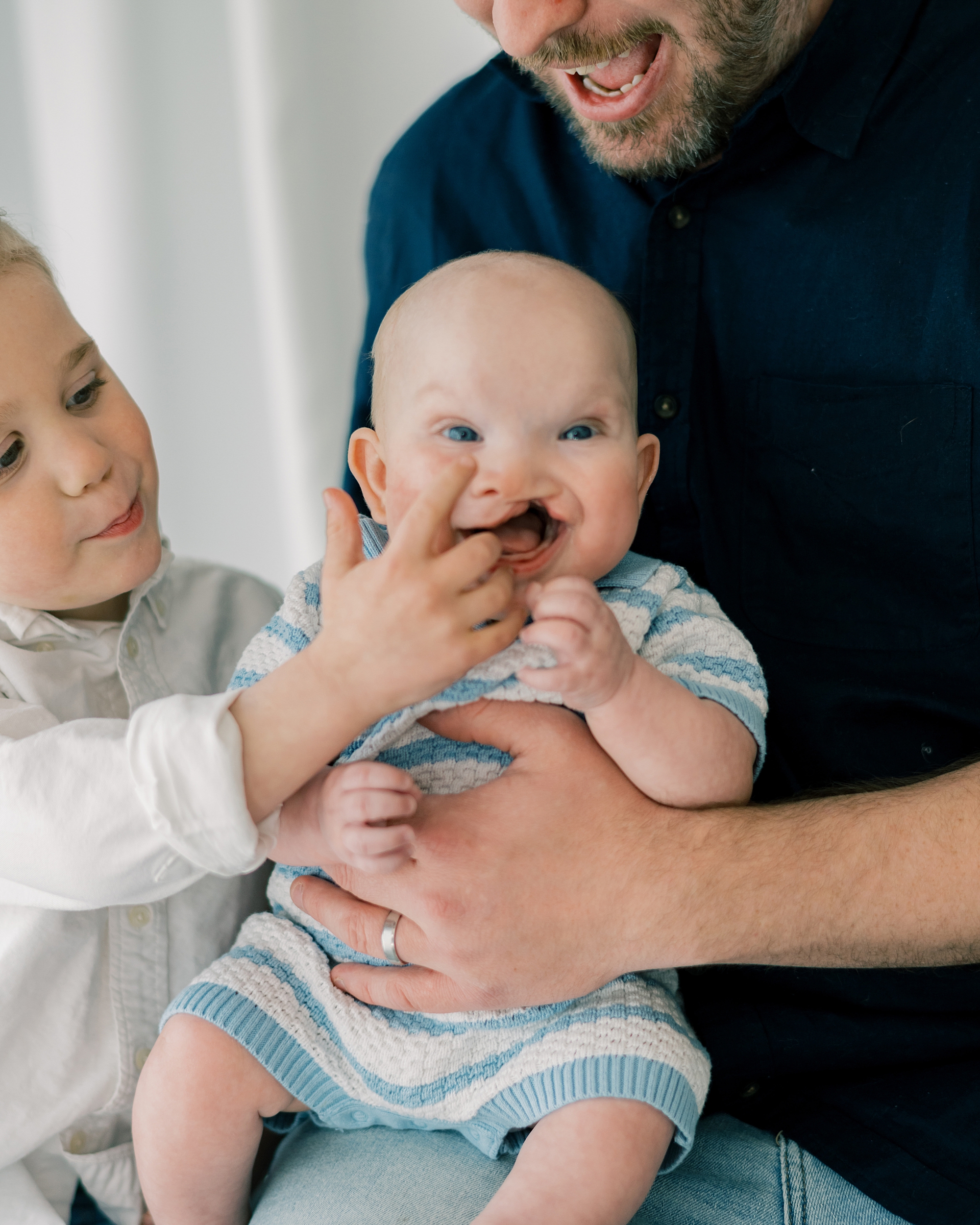 toddler boy reaches to tap baby brother's nose during milestone session in Southern Maryland studio