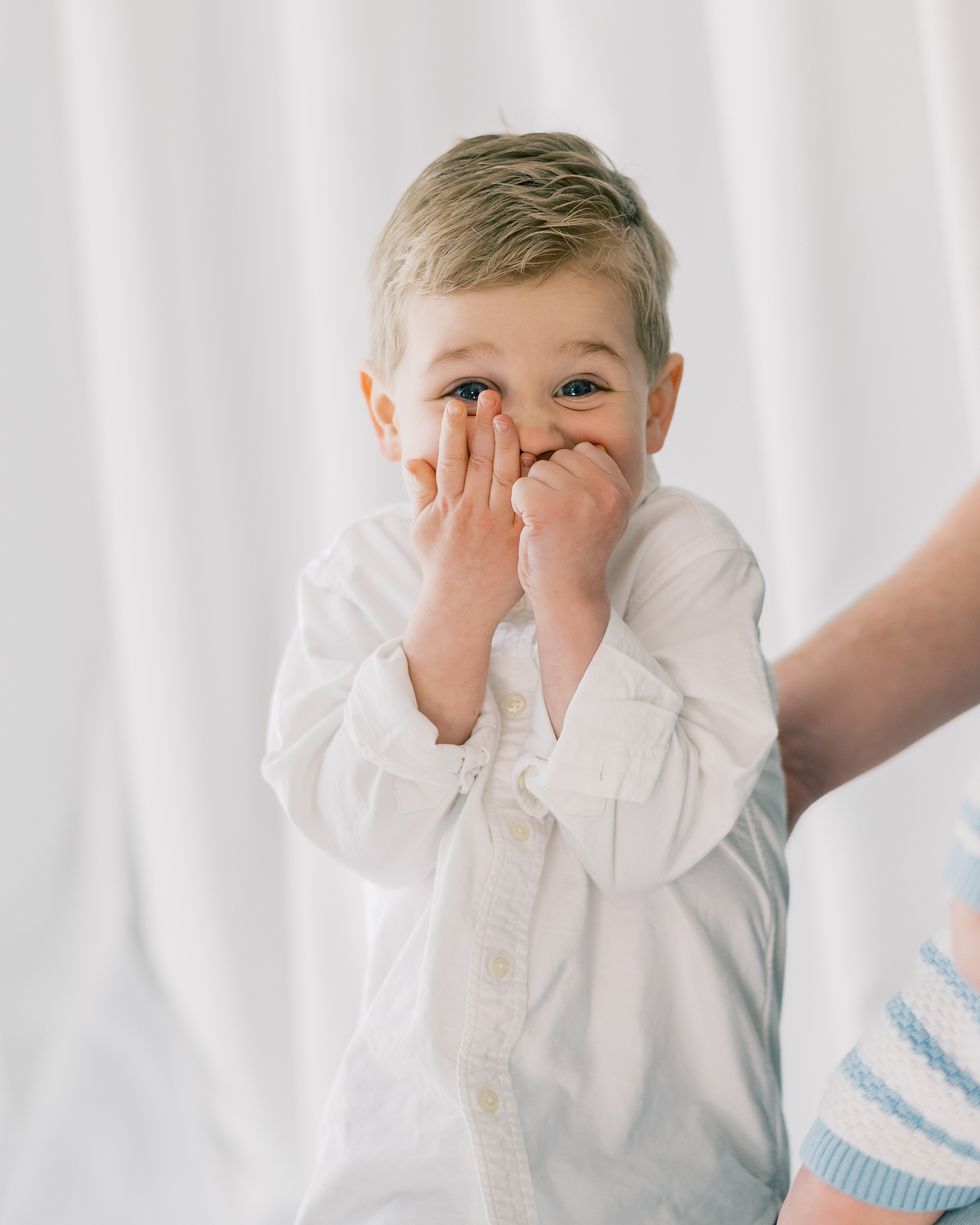 toddler in white button up shirt covers mouth laughing