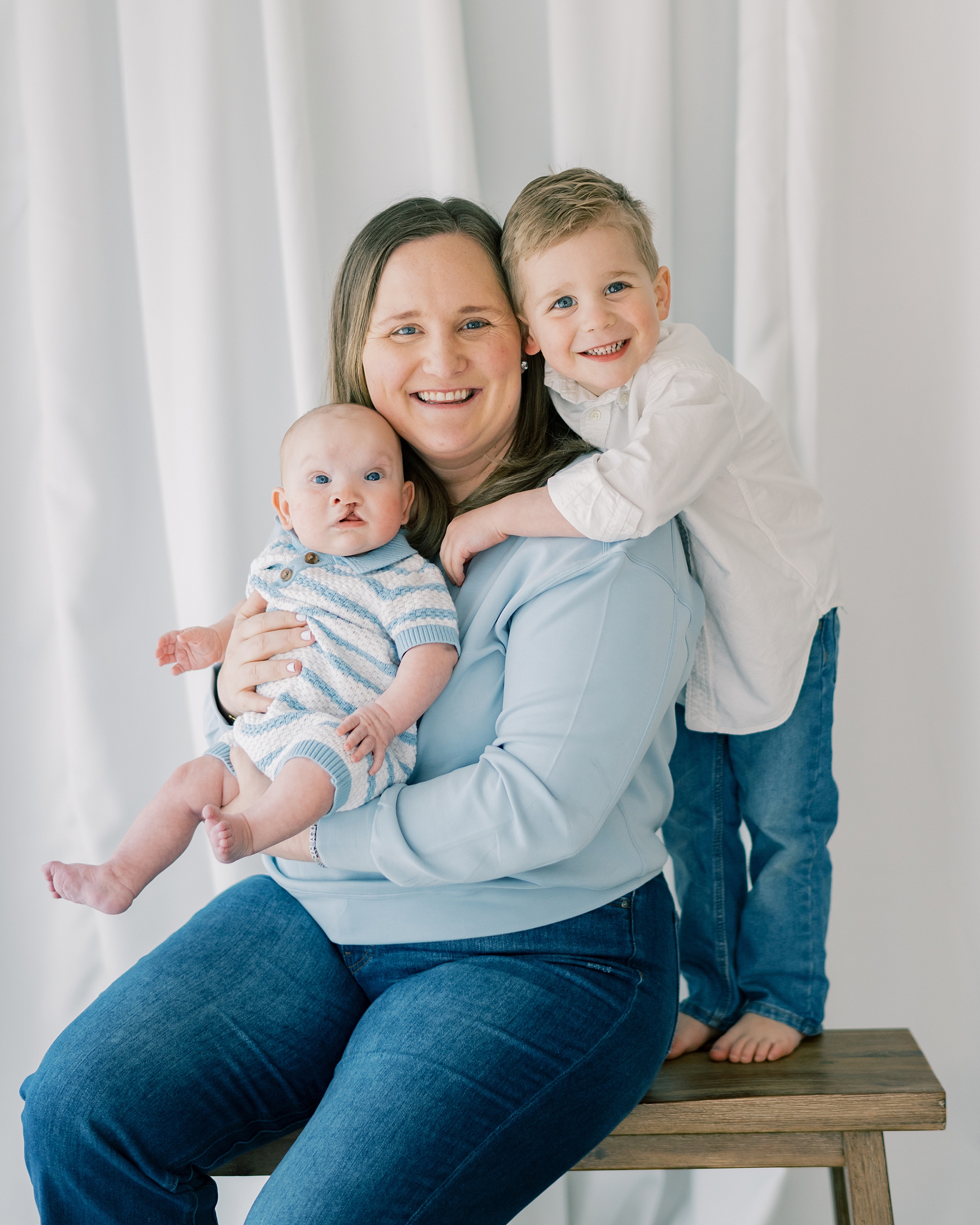 mom holds son while toddler hugs her shoulders from behind