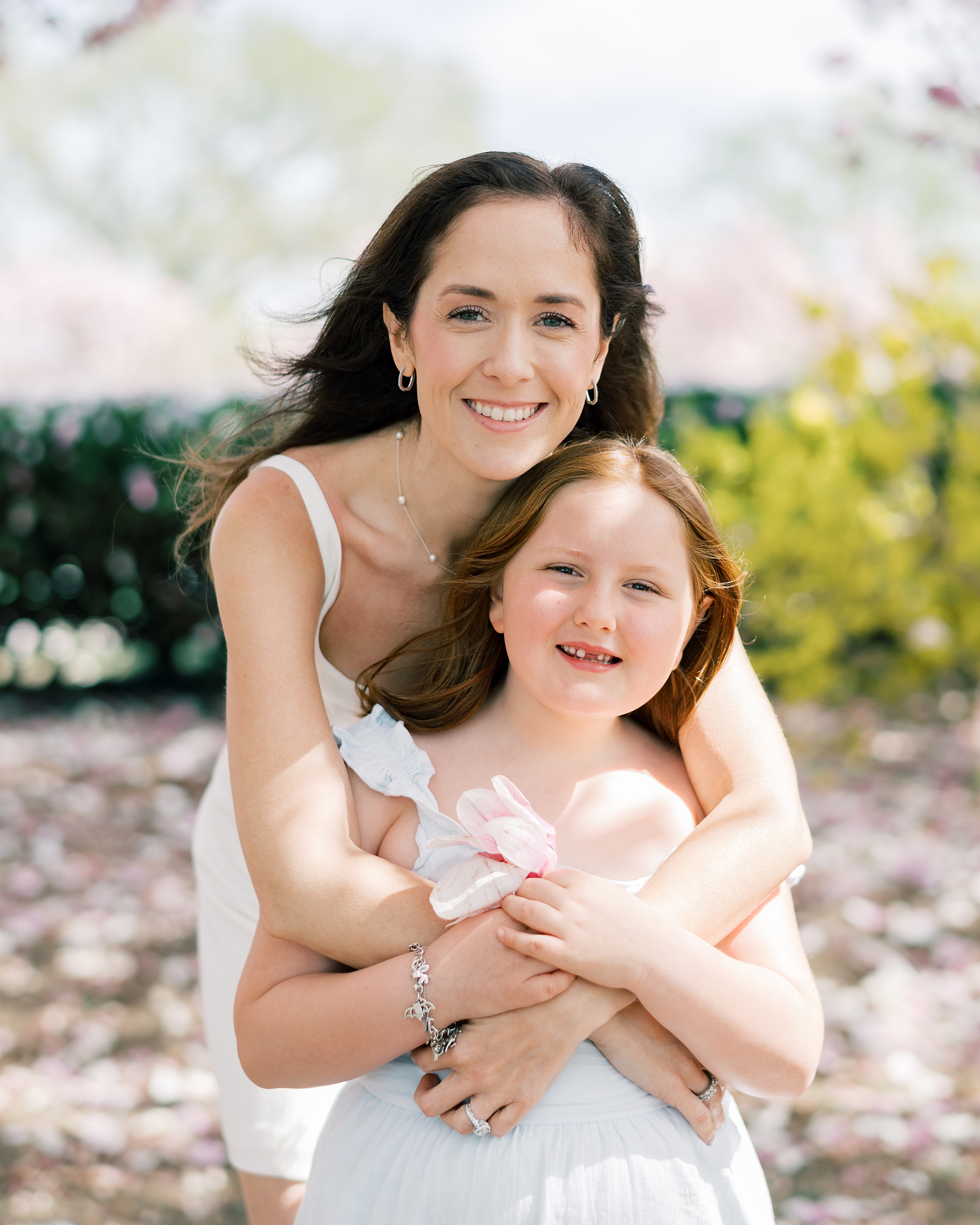 woman hugs daughter from behind during cherry blossom family portraits in Washington DC