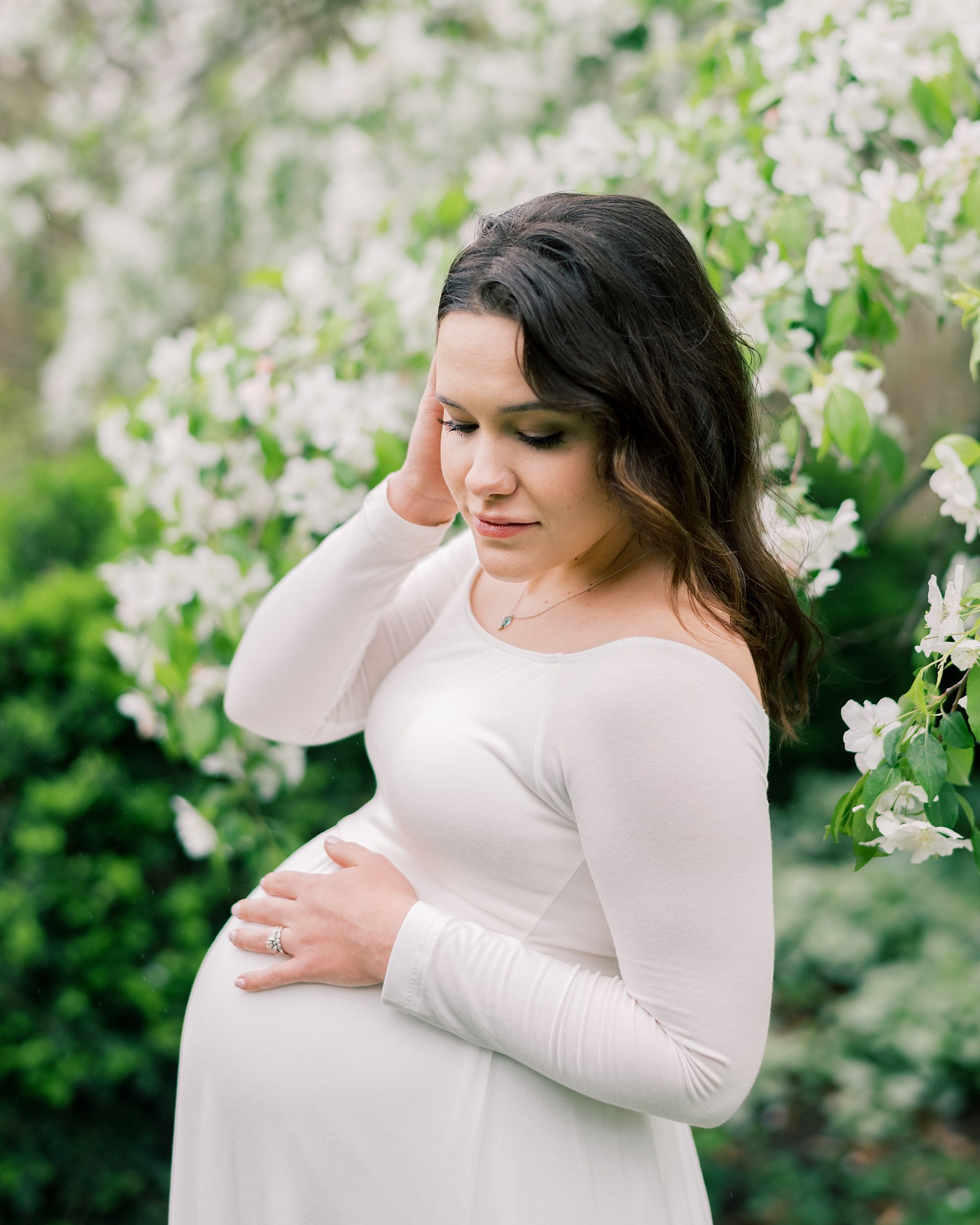 expecting mother in white dress poses in front of white flowers in trees