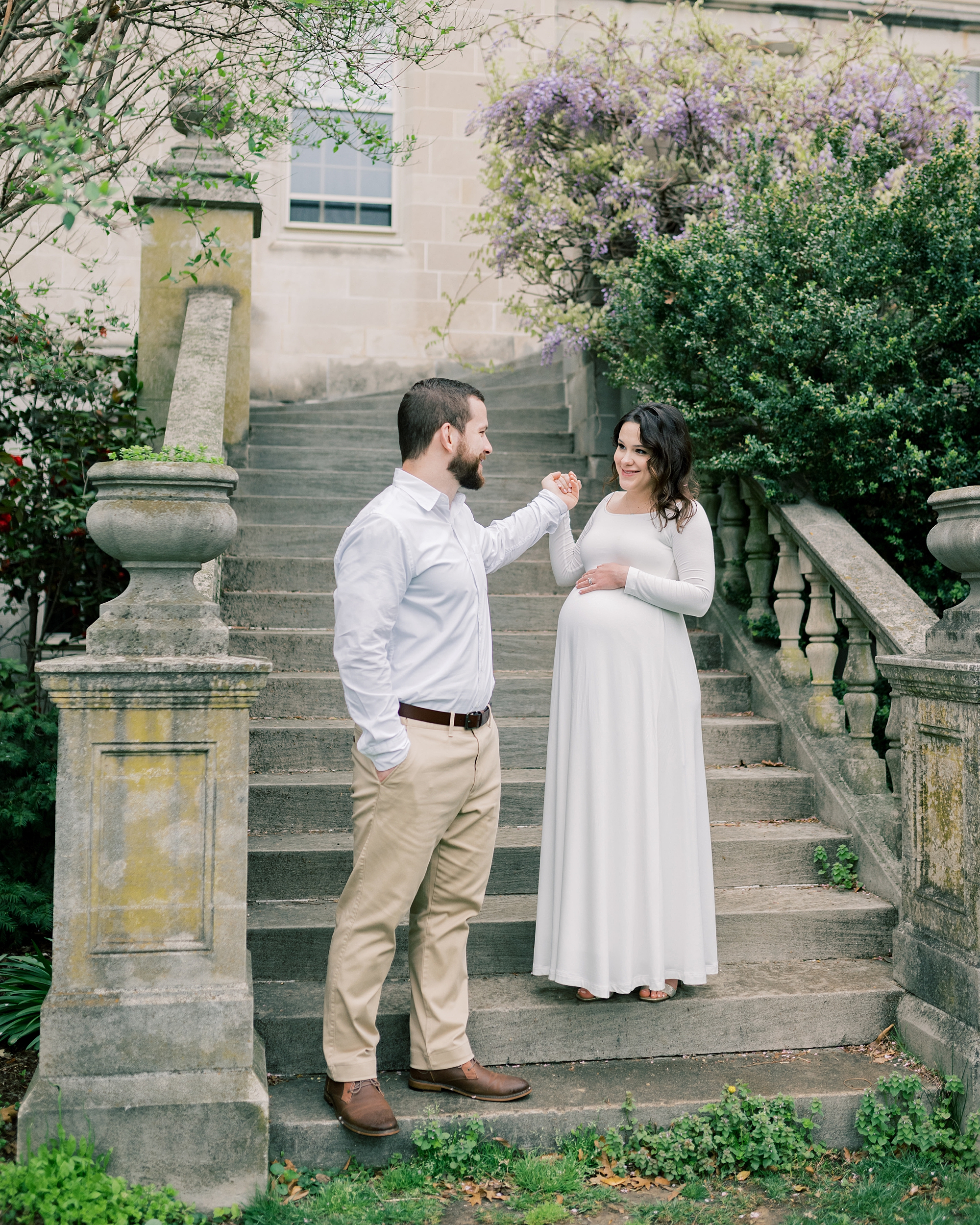 man leads expecting wife down steps during maternity session at the Washington National Cathedral