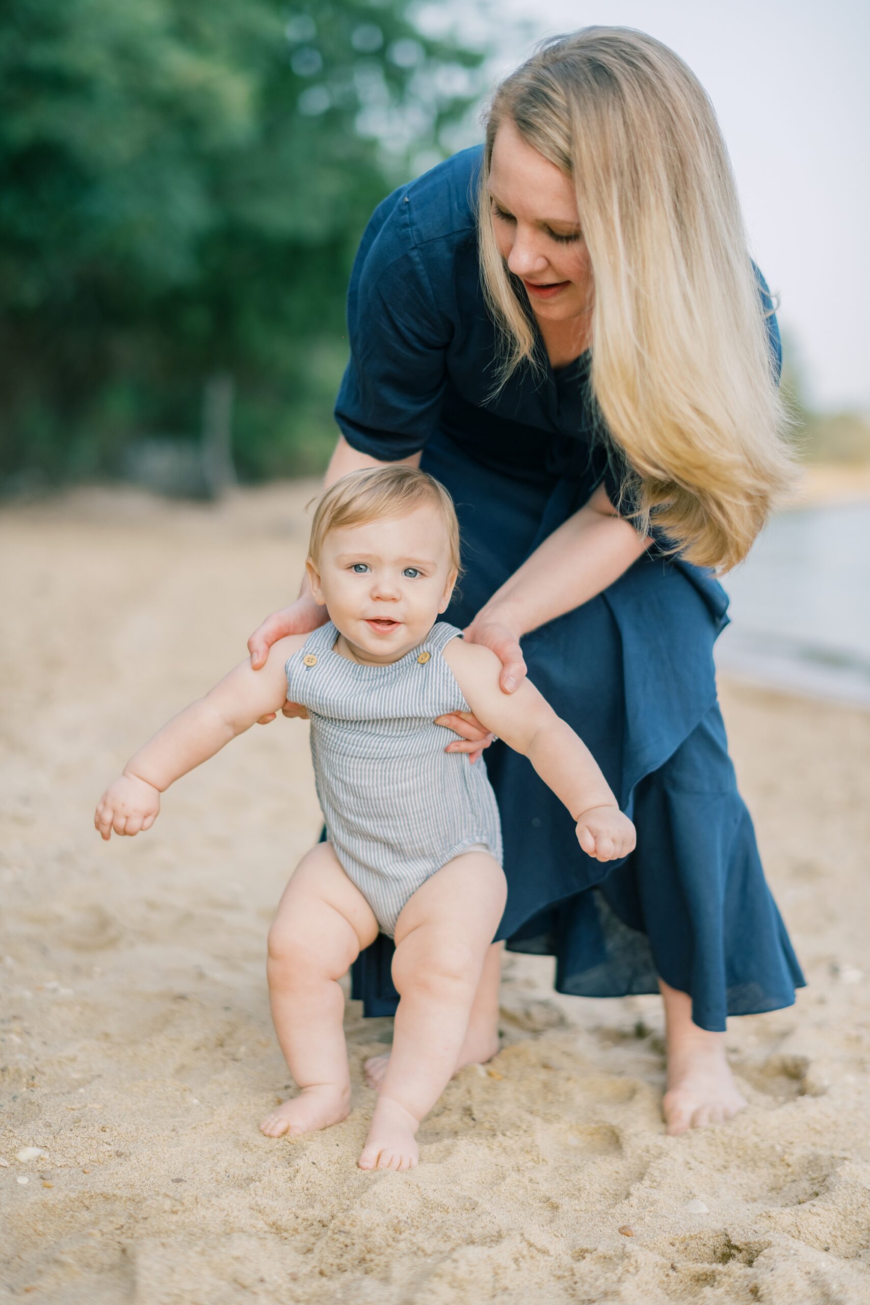 mother helps baby on beach during family photos
