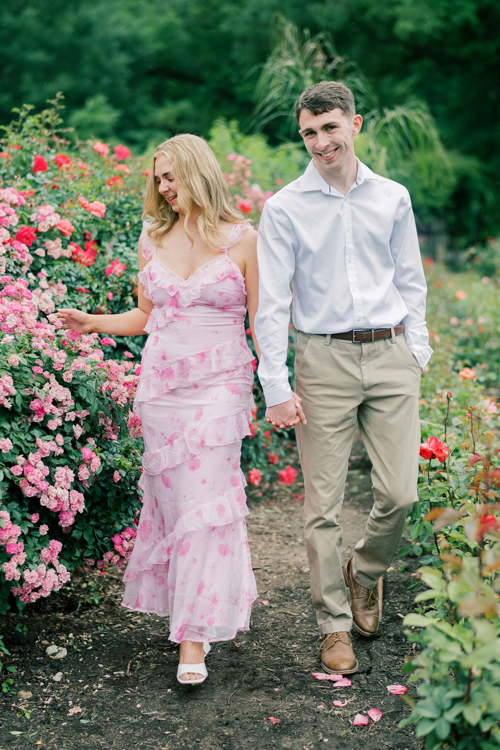 engaged couple holds hands walking through Bon Air Rose Garden