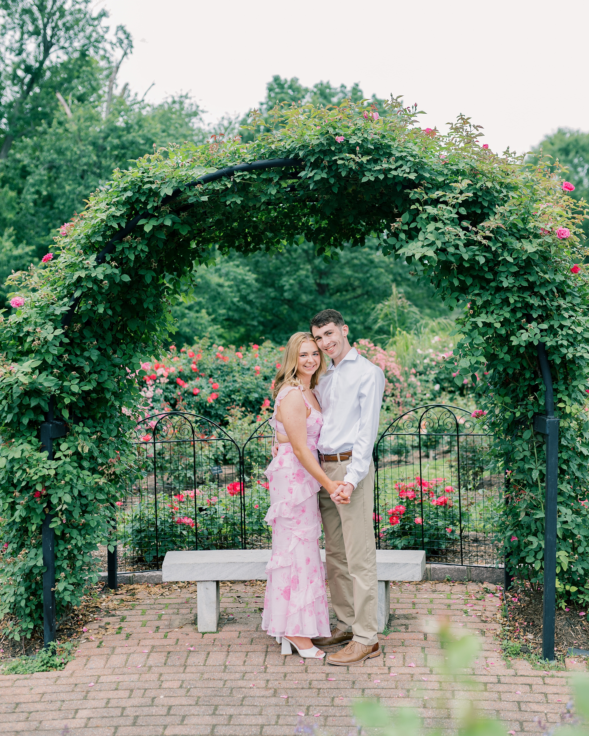 man and woman hold hands under arch during garden engagement session in Arlington VA