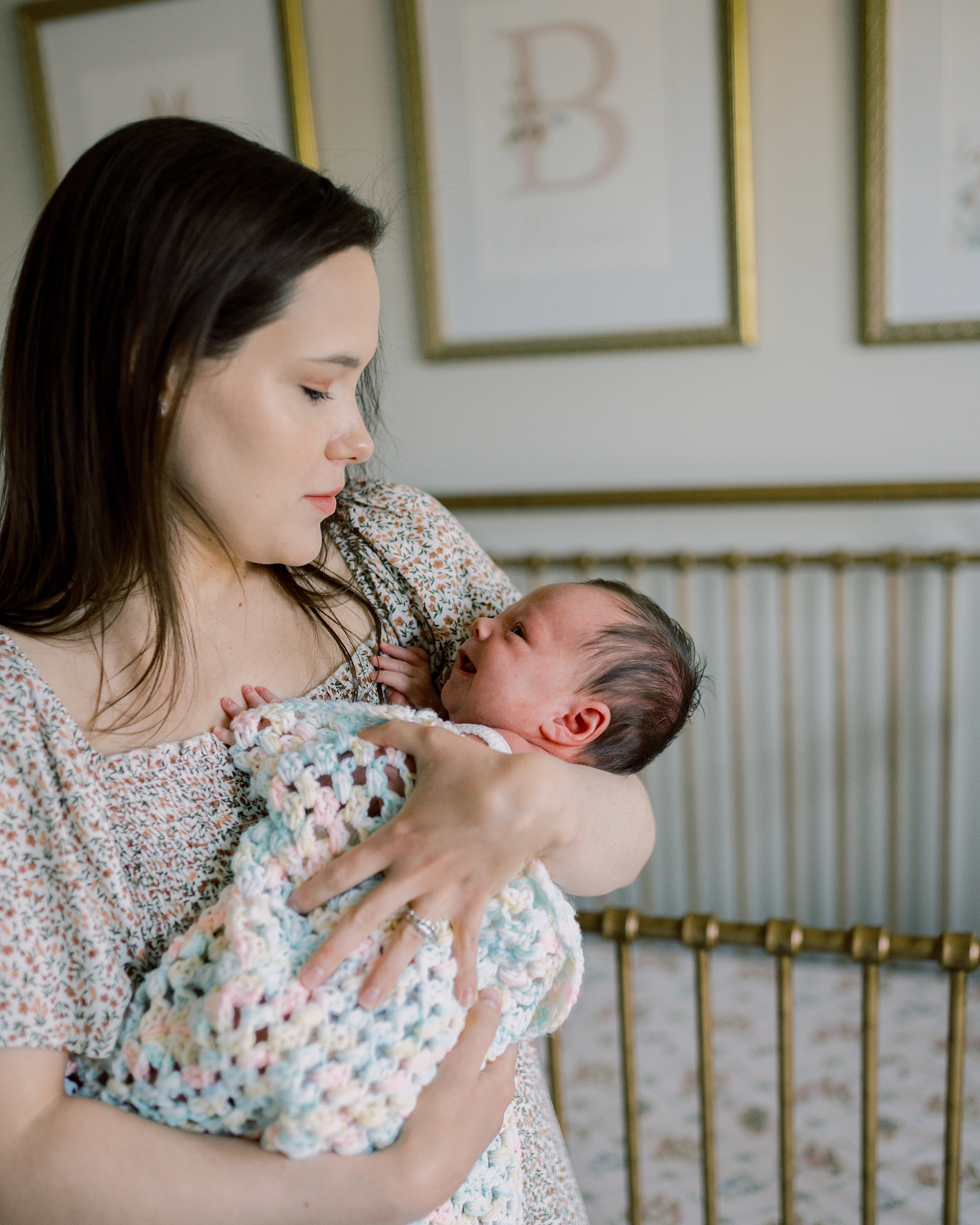 mom smiles at baby girl in front of gold metal crib during newborn session at home in Washington DC
