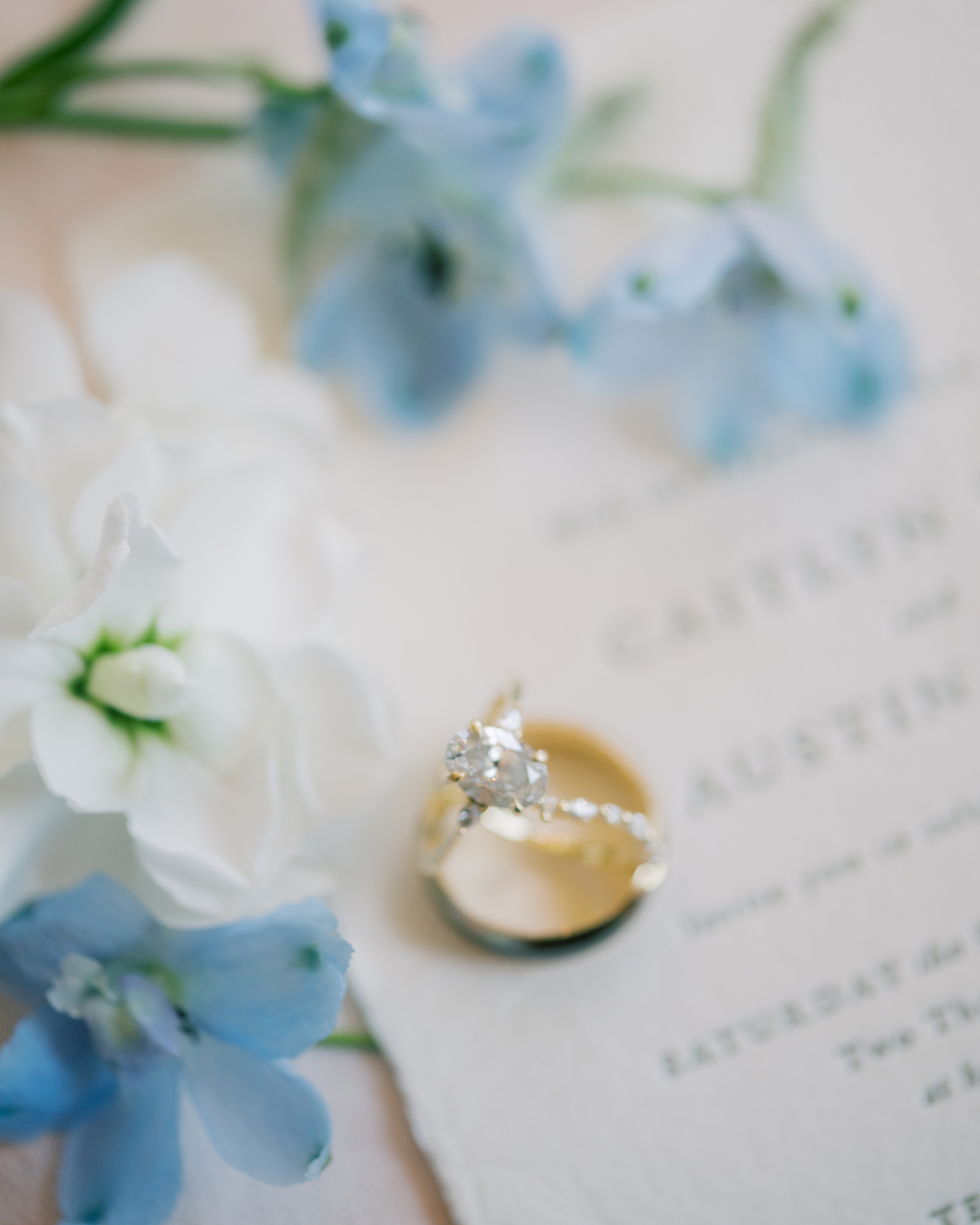 gold wedding bands rest on blue and white invitation suite