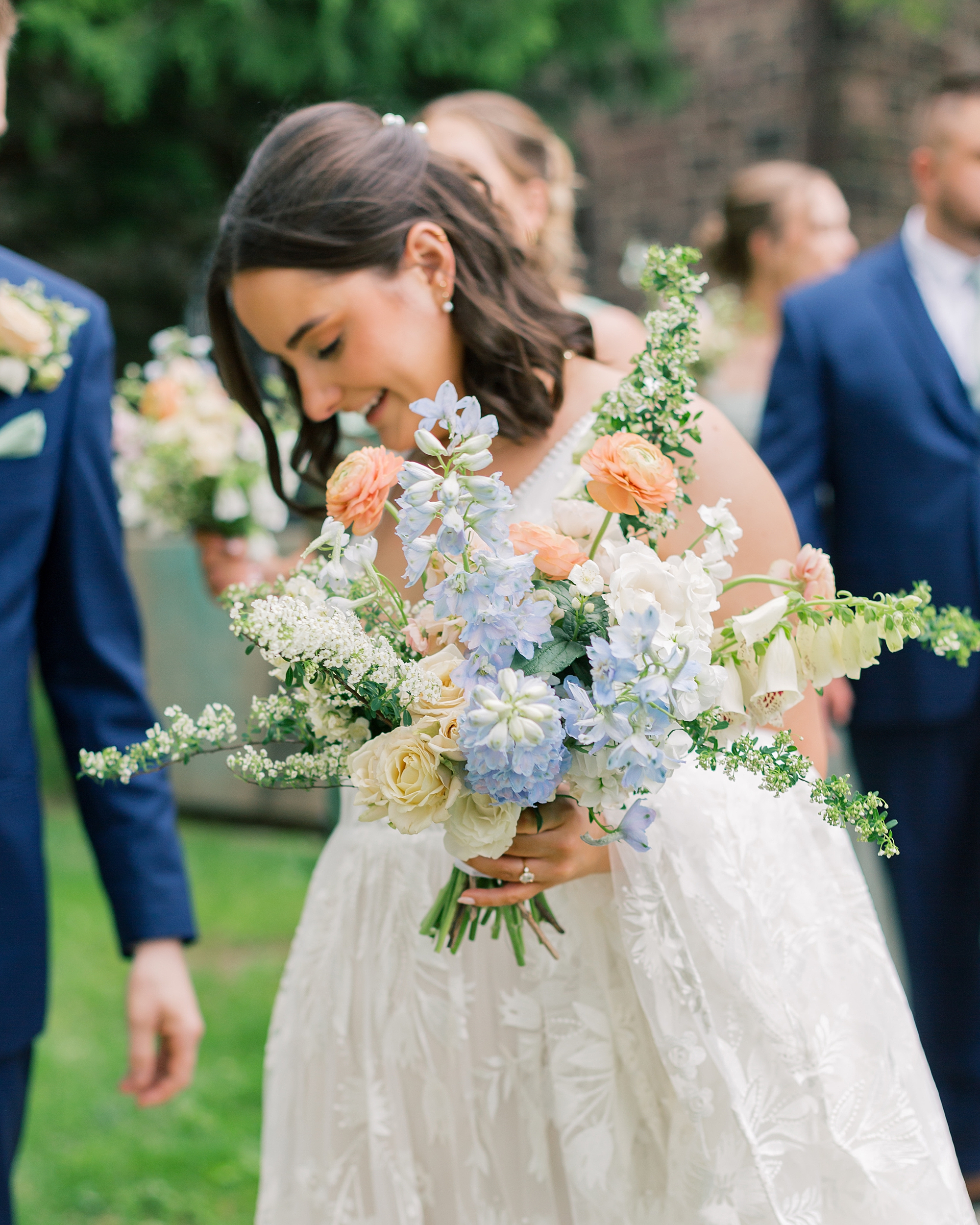 bride walks carrying spring bouquet of peach and blue flowers