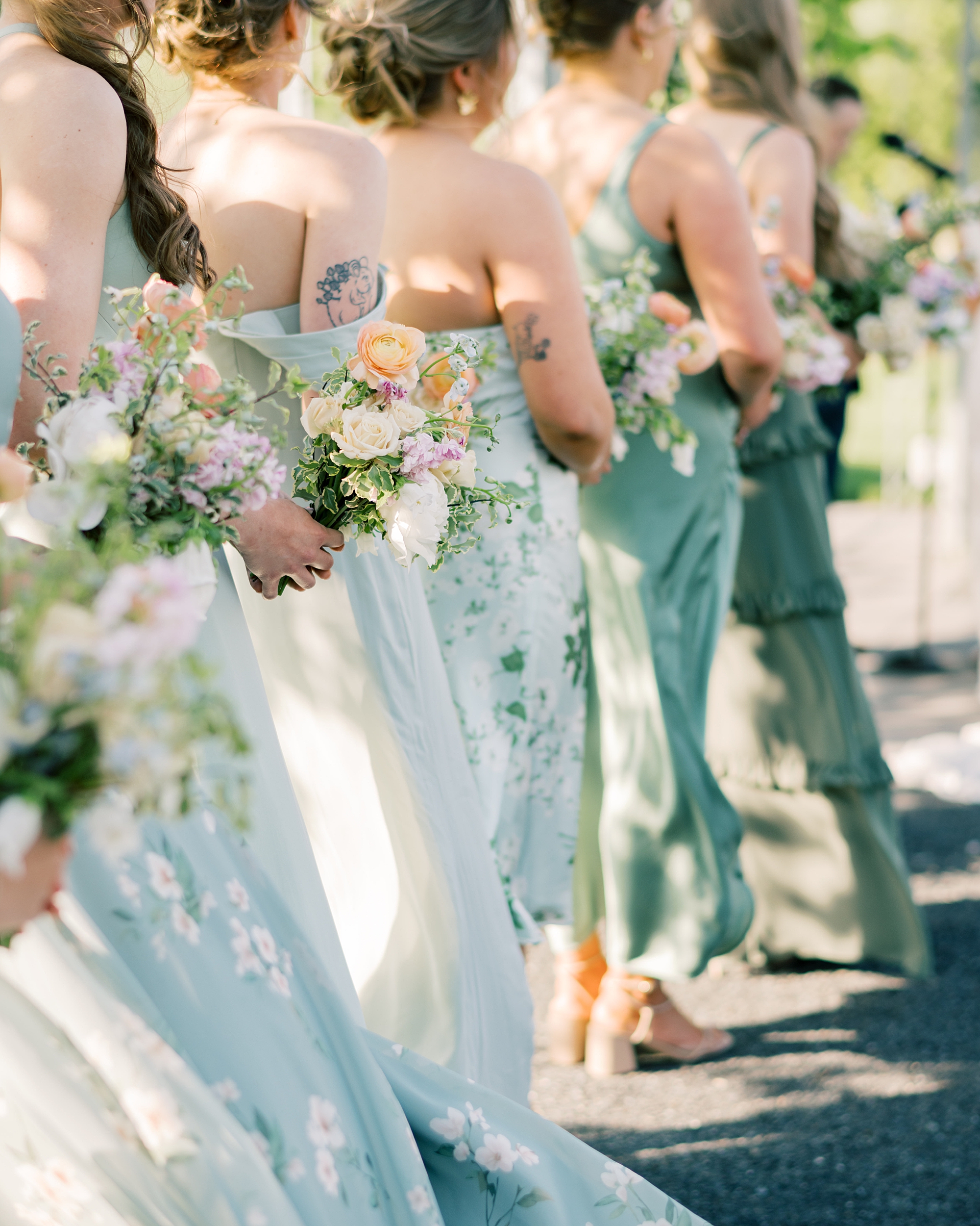 bridesmaids stand in mismatched blue and green gowns for wedding ceremony at Terrain Gardens