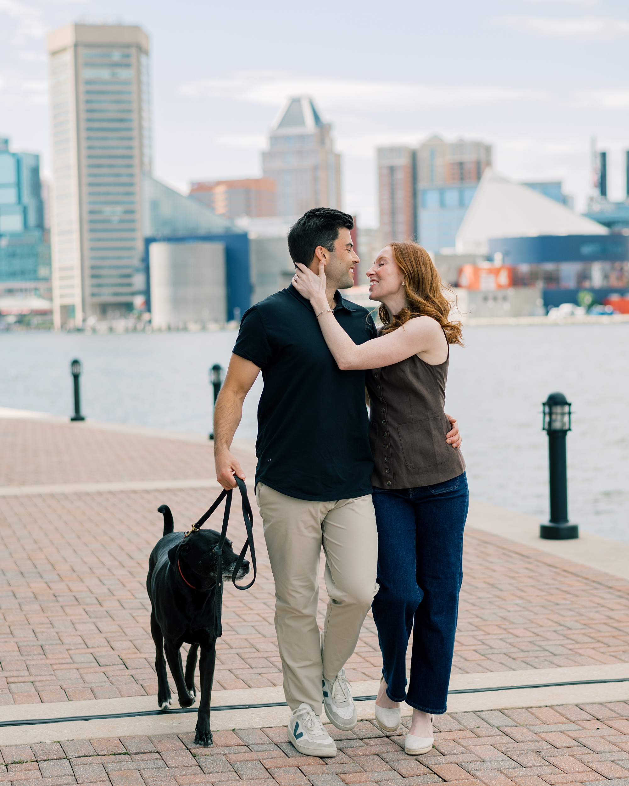 engaged couple hugs walking dog through Inner Harbor Baltimore