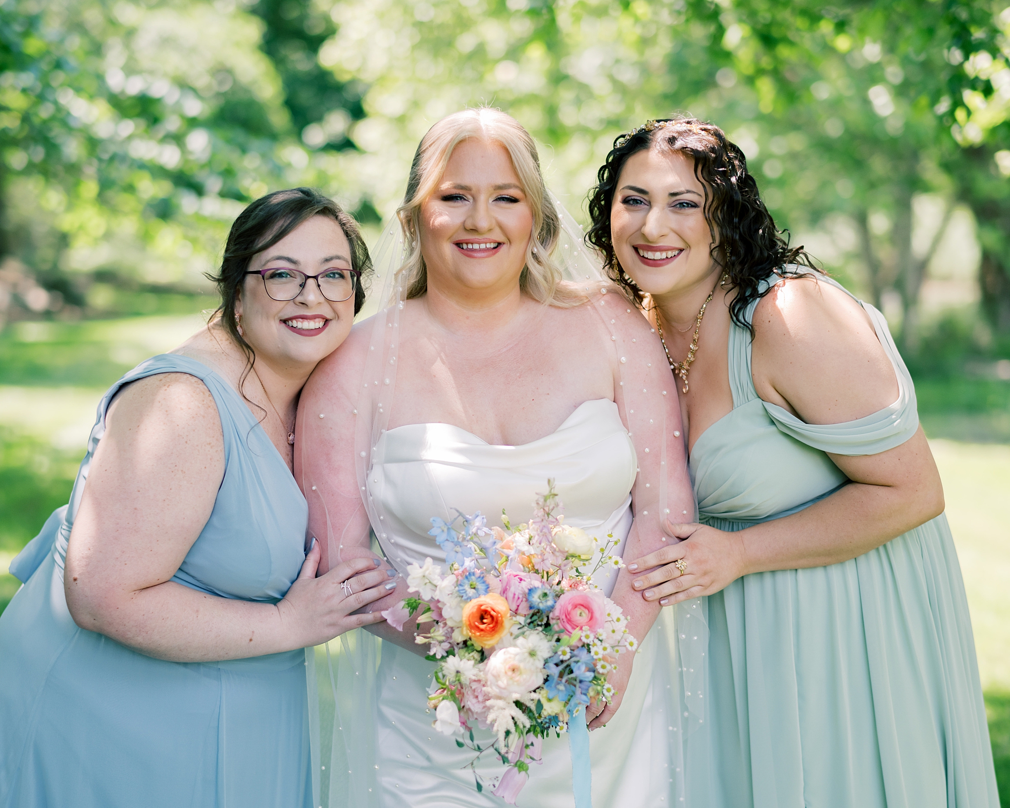 bridesmaids in pastel gowns lean into bride with pastel bouquet 