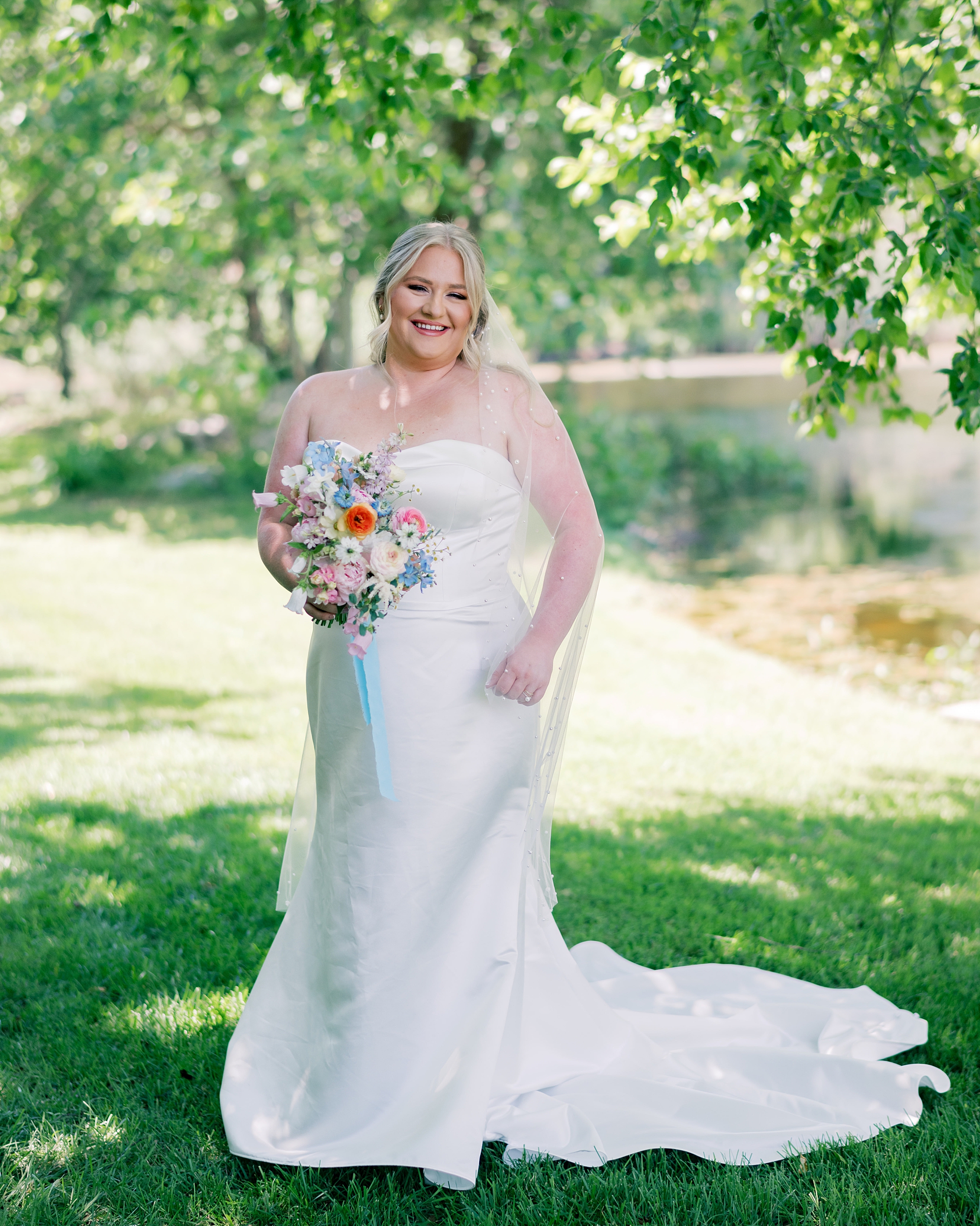 bride stands holding pastel flowers in strapless wedding gown 