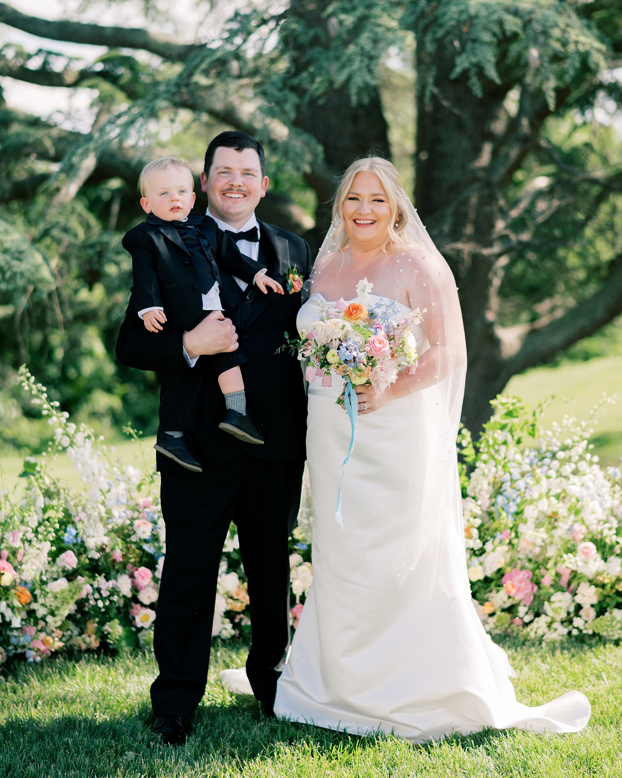 bride and groom stand at ceremony site with son