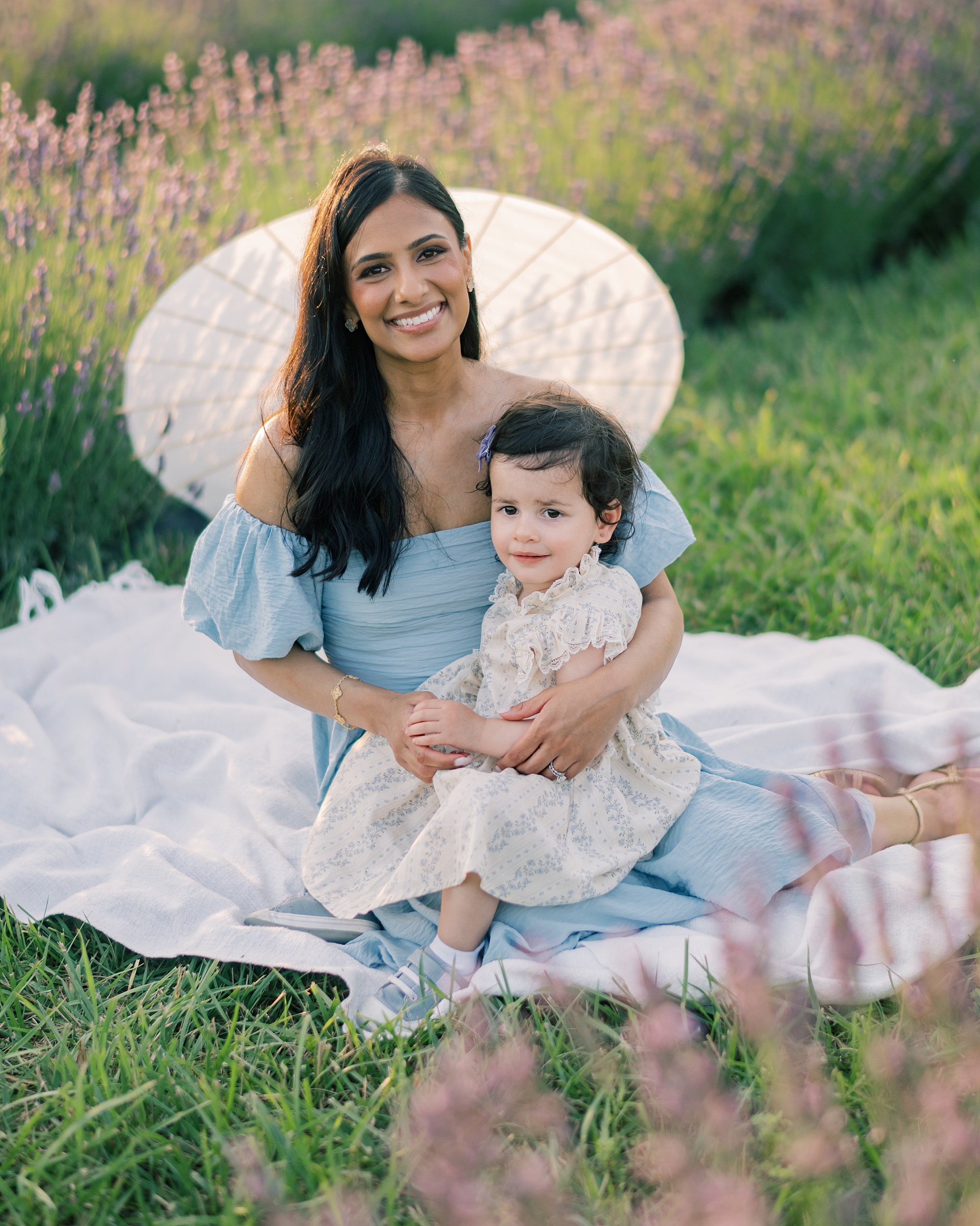 mother sits on blanket with toddler holding parasol in lavender field