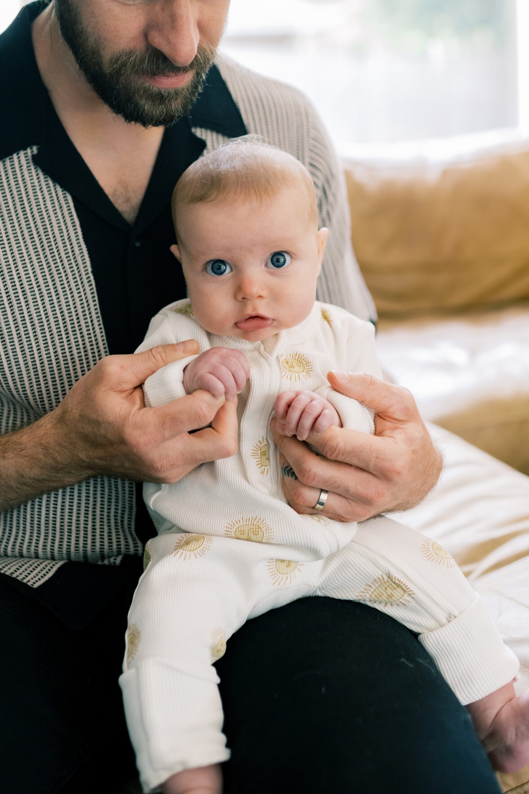 baby girl sits on dad's knee during newborn photos at home