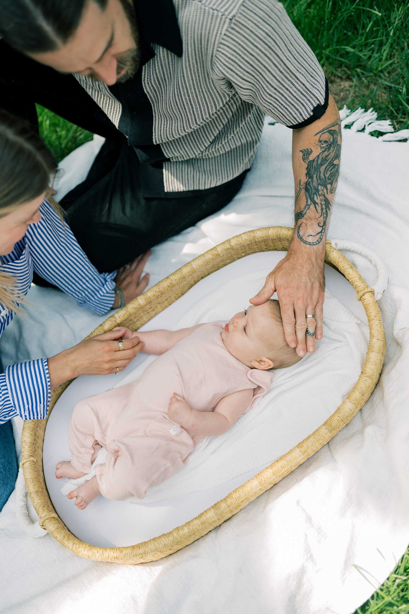 mom and dad play with daughter laying in basket in backyard