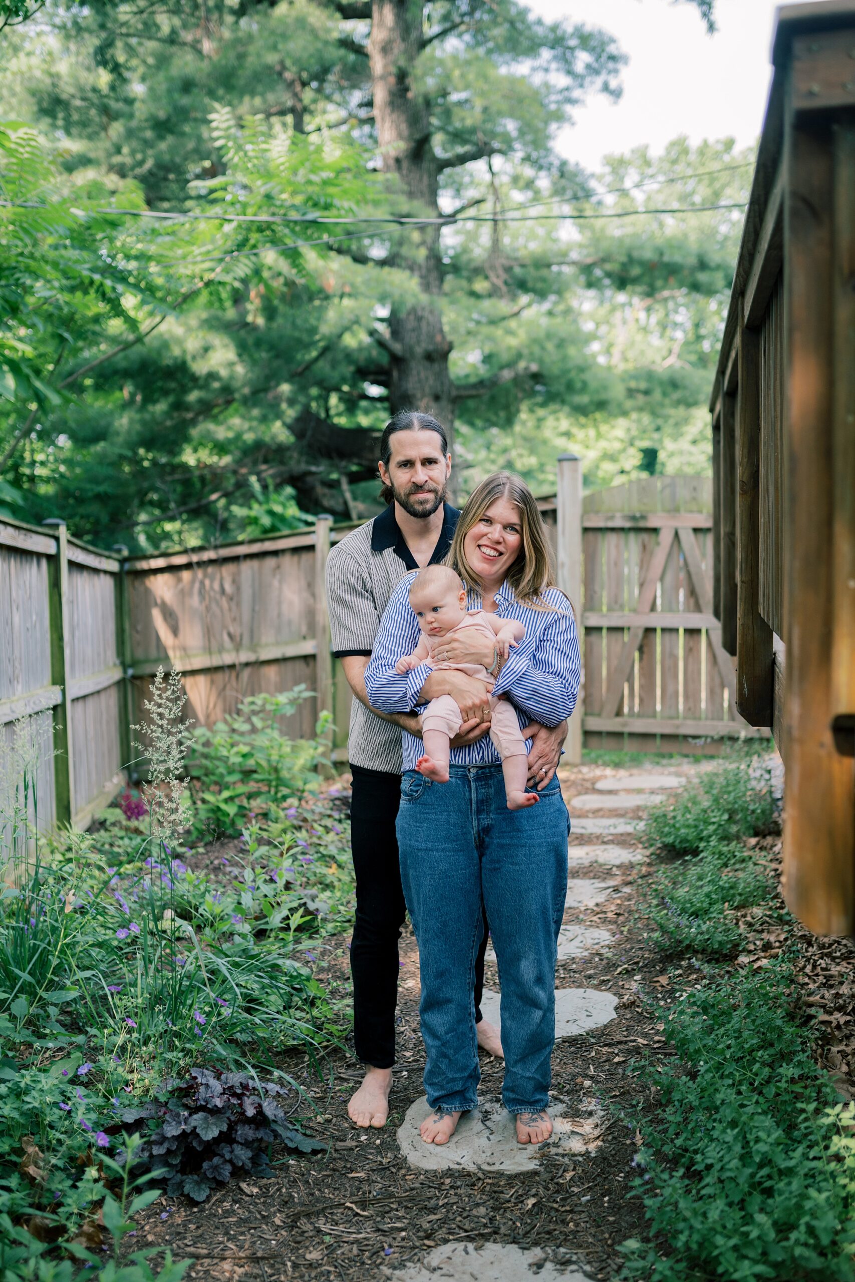 parents pose on stone walkway with daughter during newborn session in Washington DC home