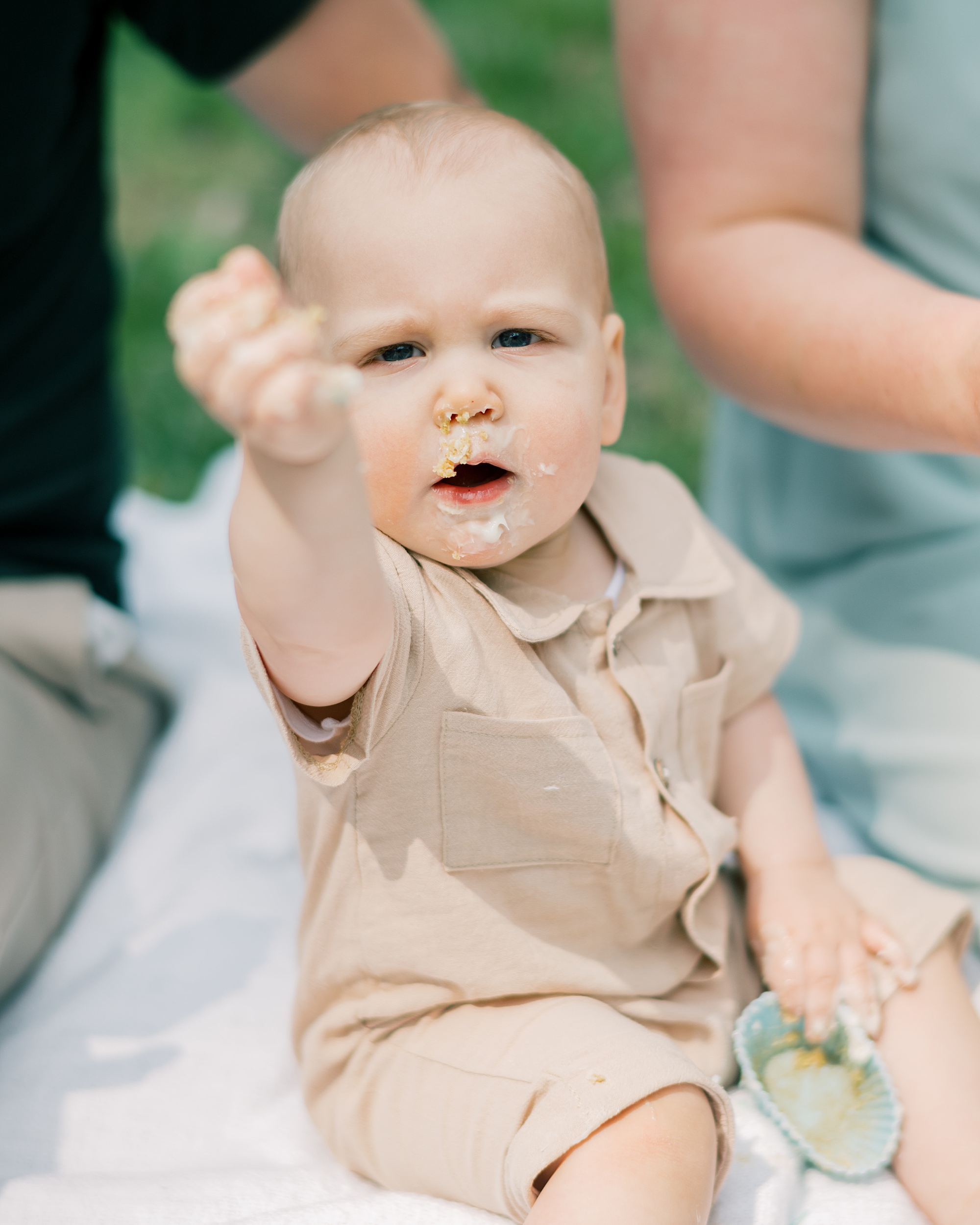 baby holds up hand covered in icing during first birthday session