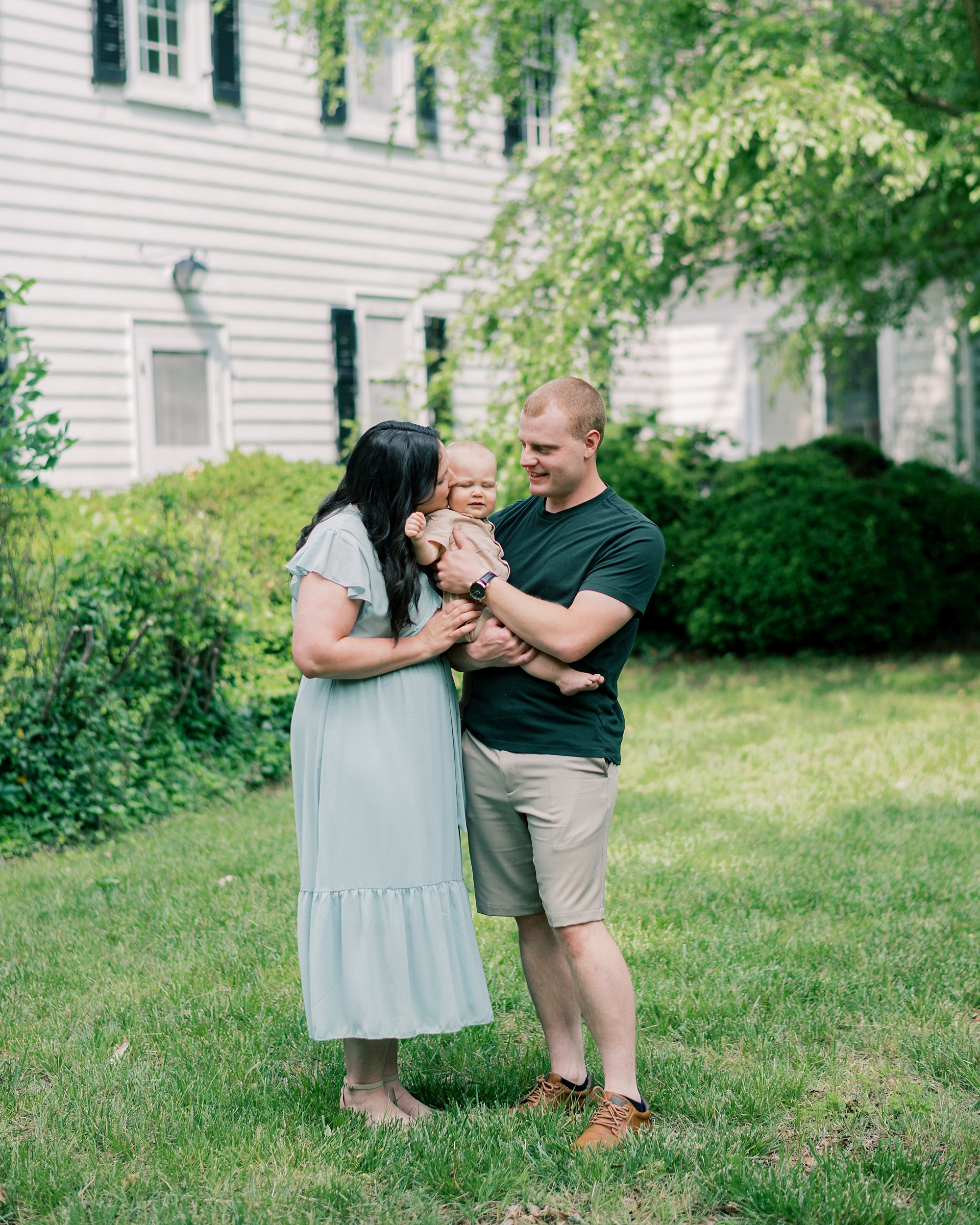 parents snuggle with one year old son on lawn of Maryland home