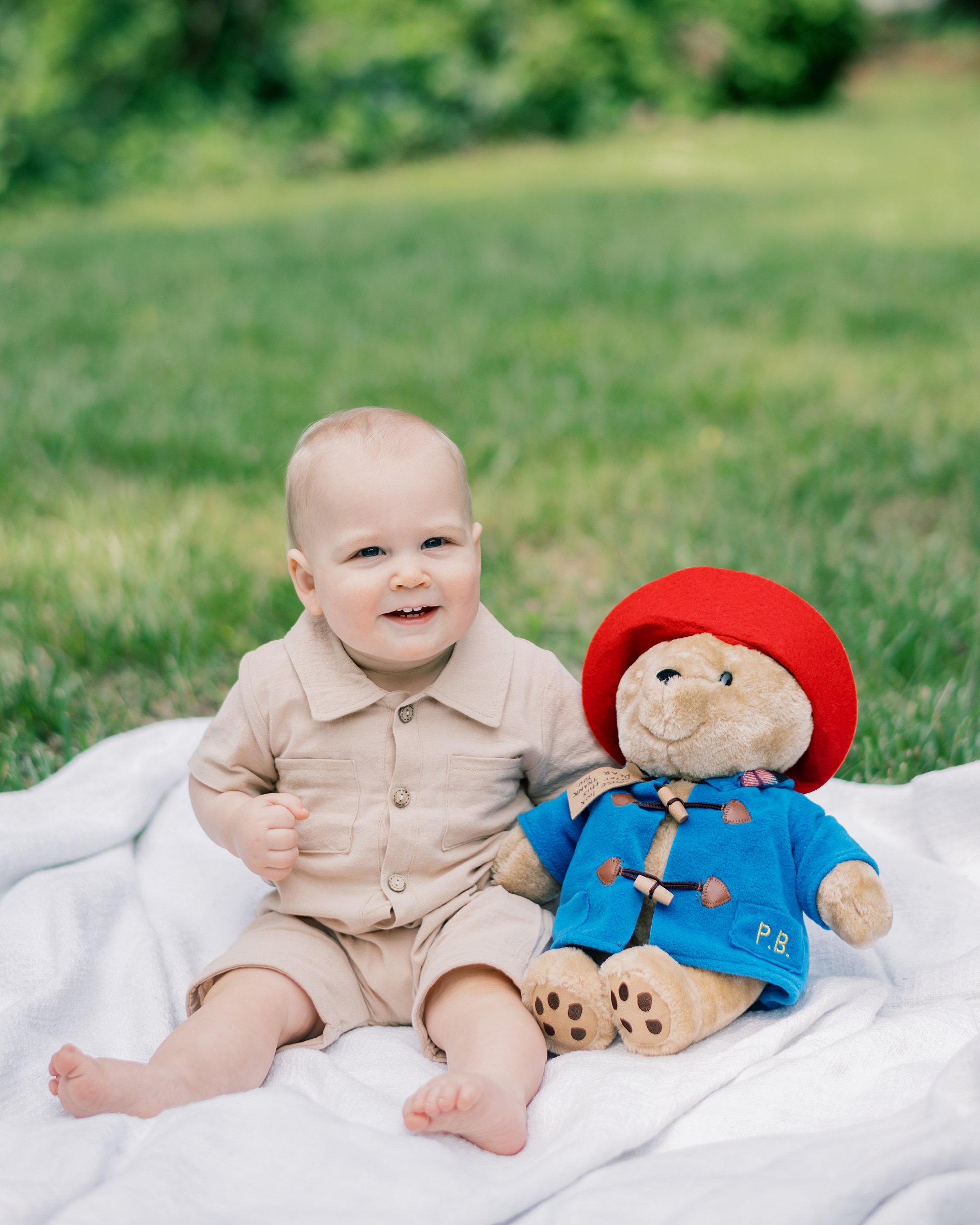 one year old sits by Paddington bear doll on blanket
