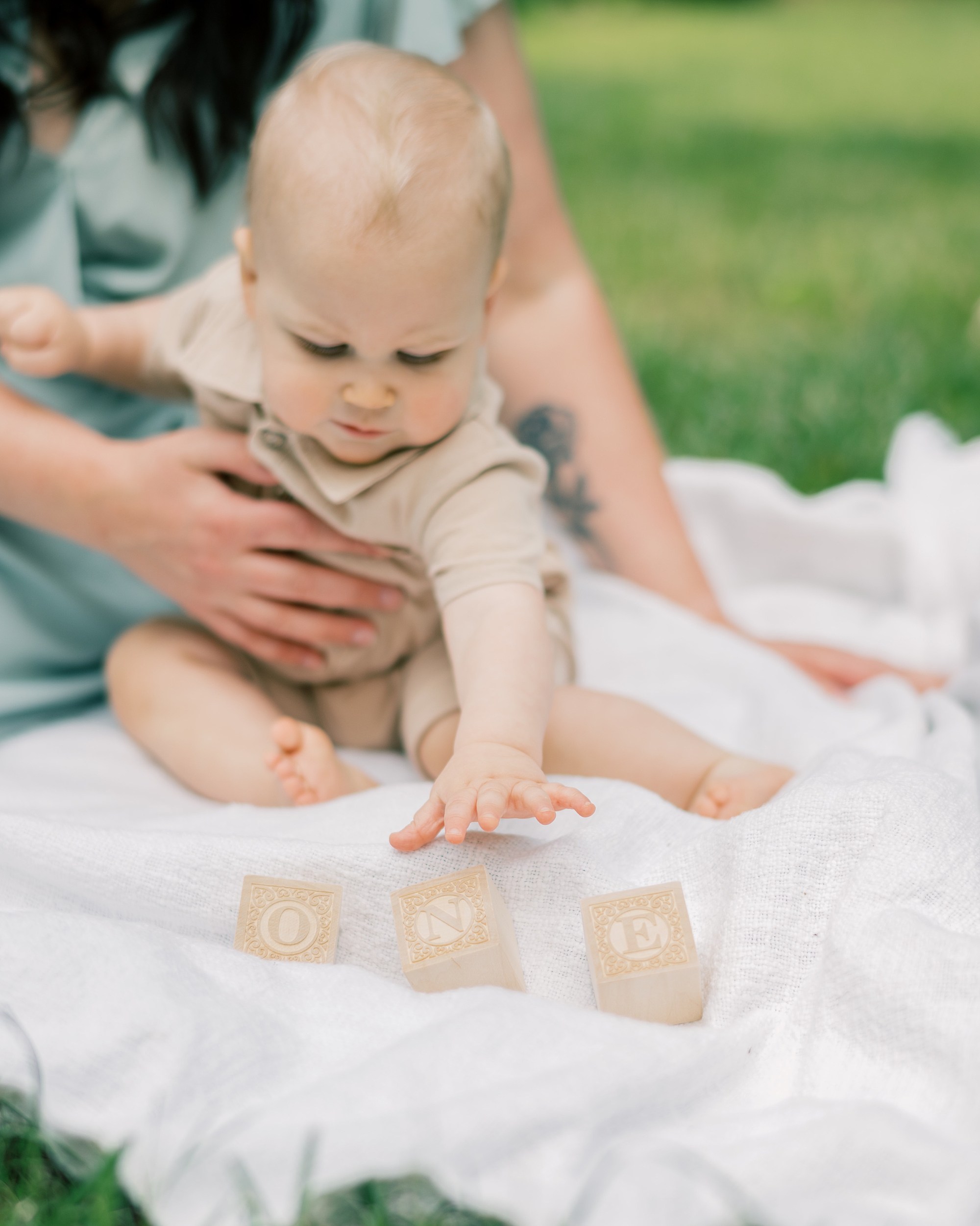 toddler sits on white blanket with wooden blocks