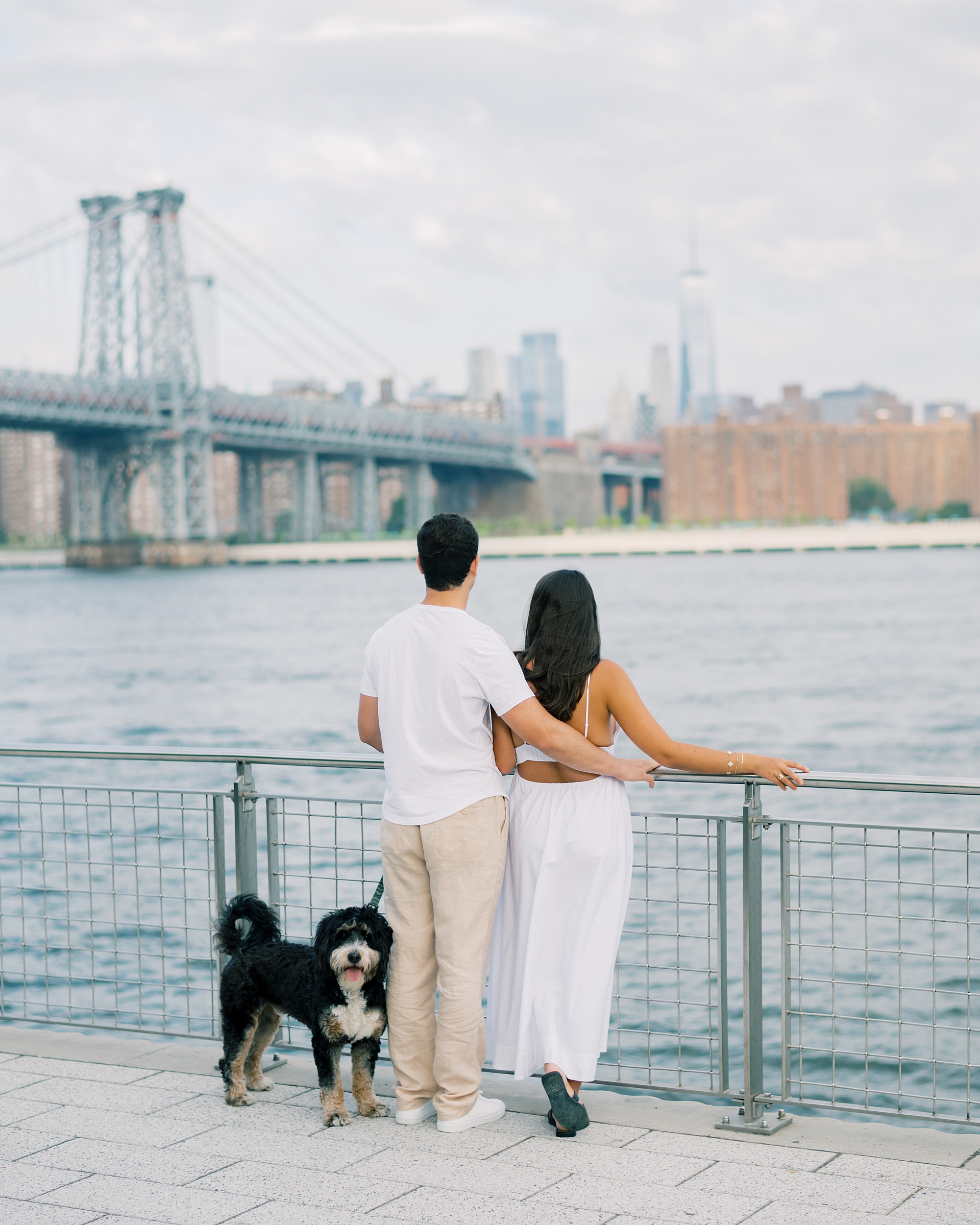 man hugs woman against railing at Domino Park