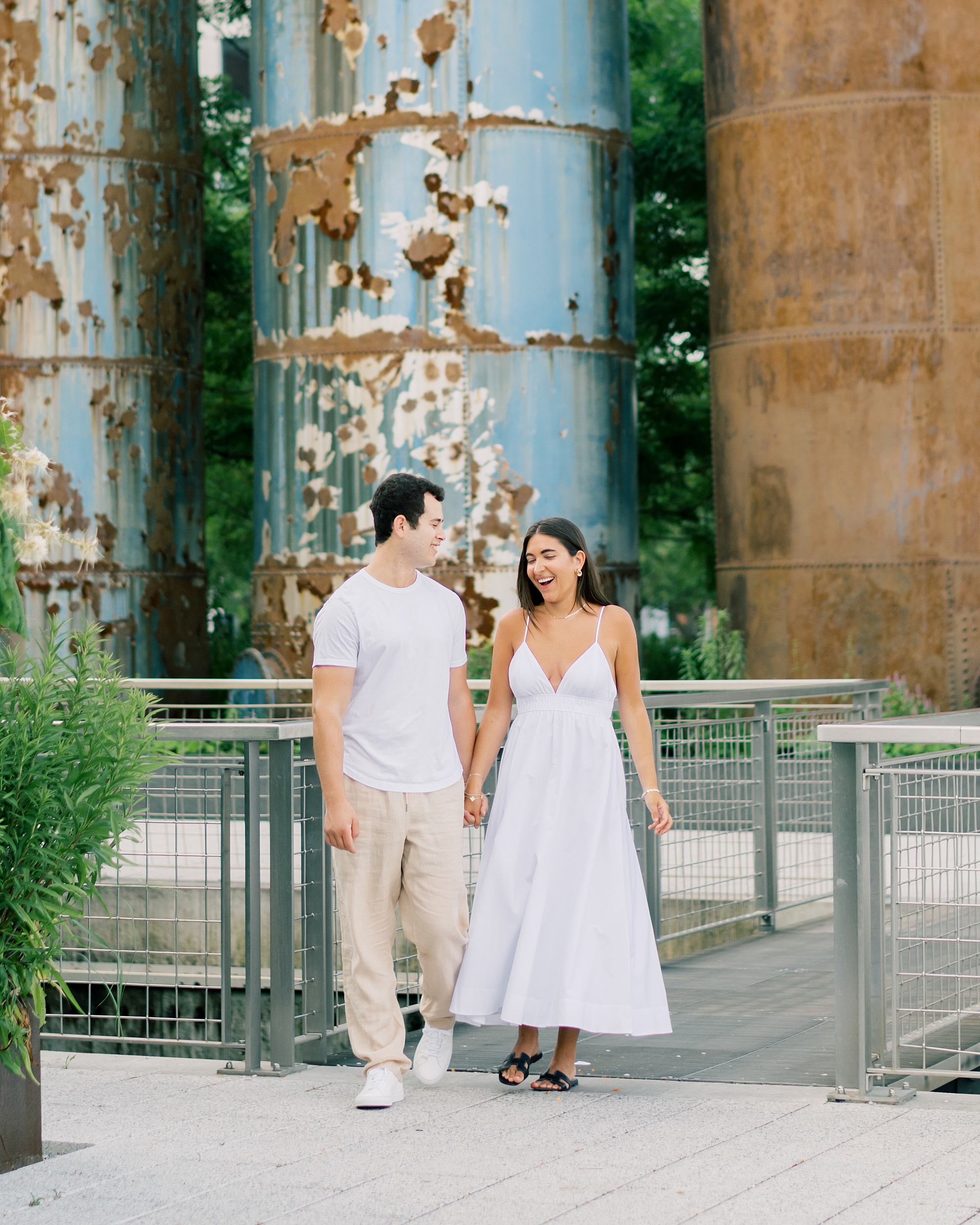 man and woman hold hands walking in front of old smoke stacks 