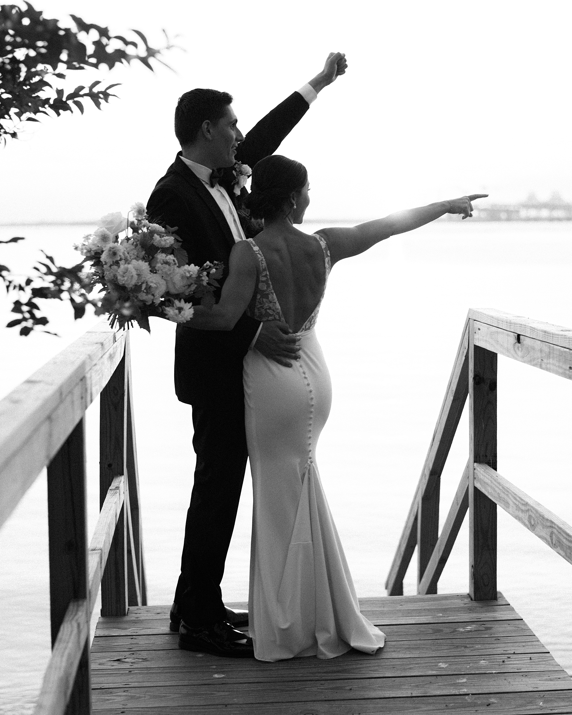 bride and groom point at boat on water on steps at Chesapeake Bay Beach Club