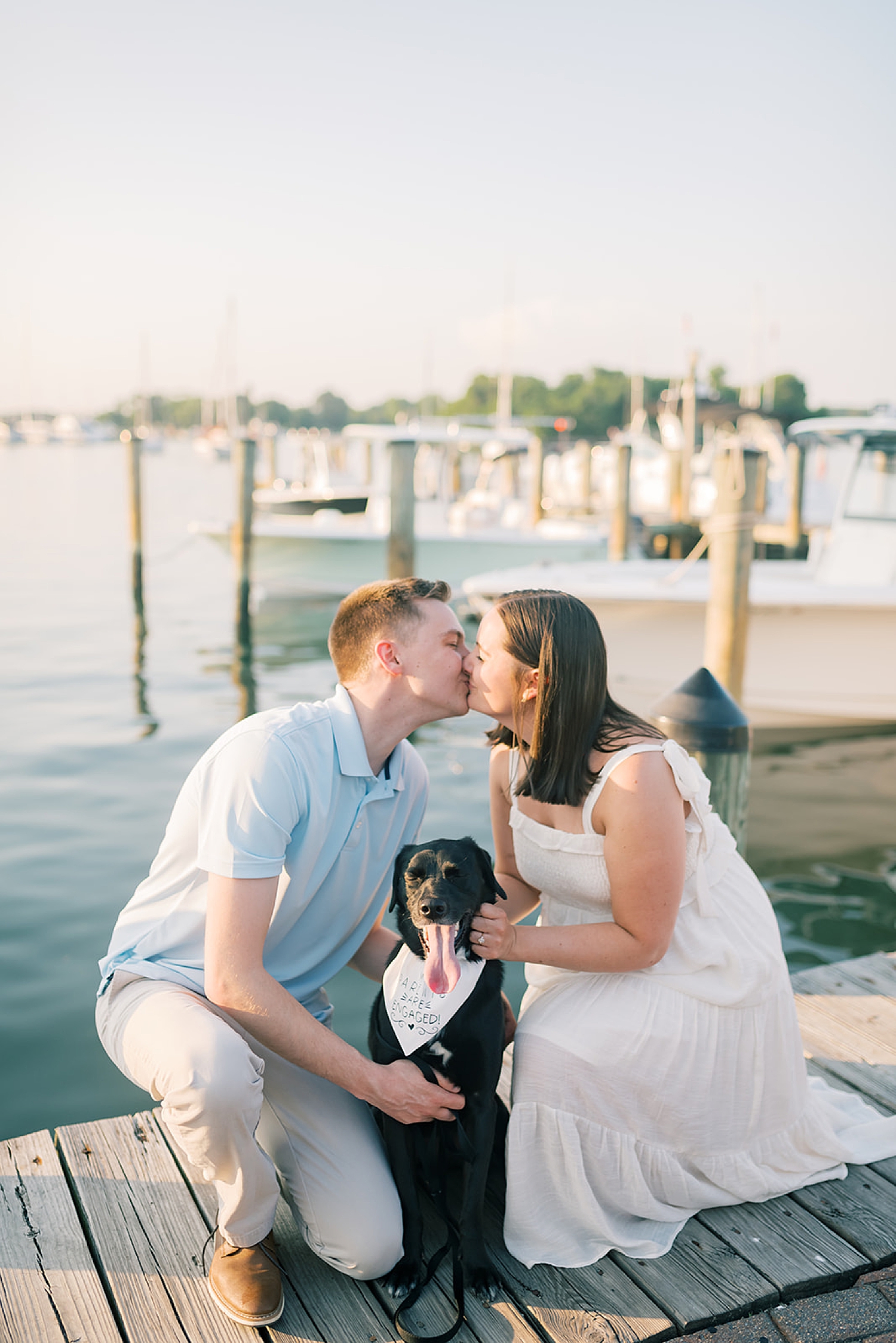 couple kiss by the water with their dog 