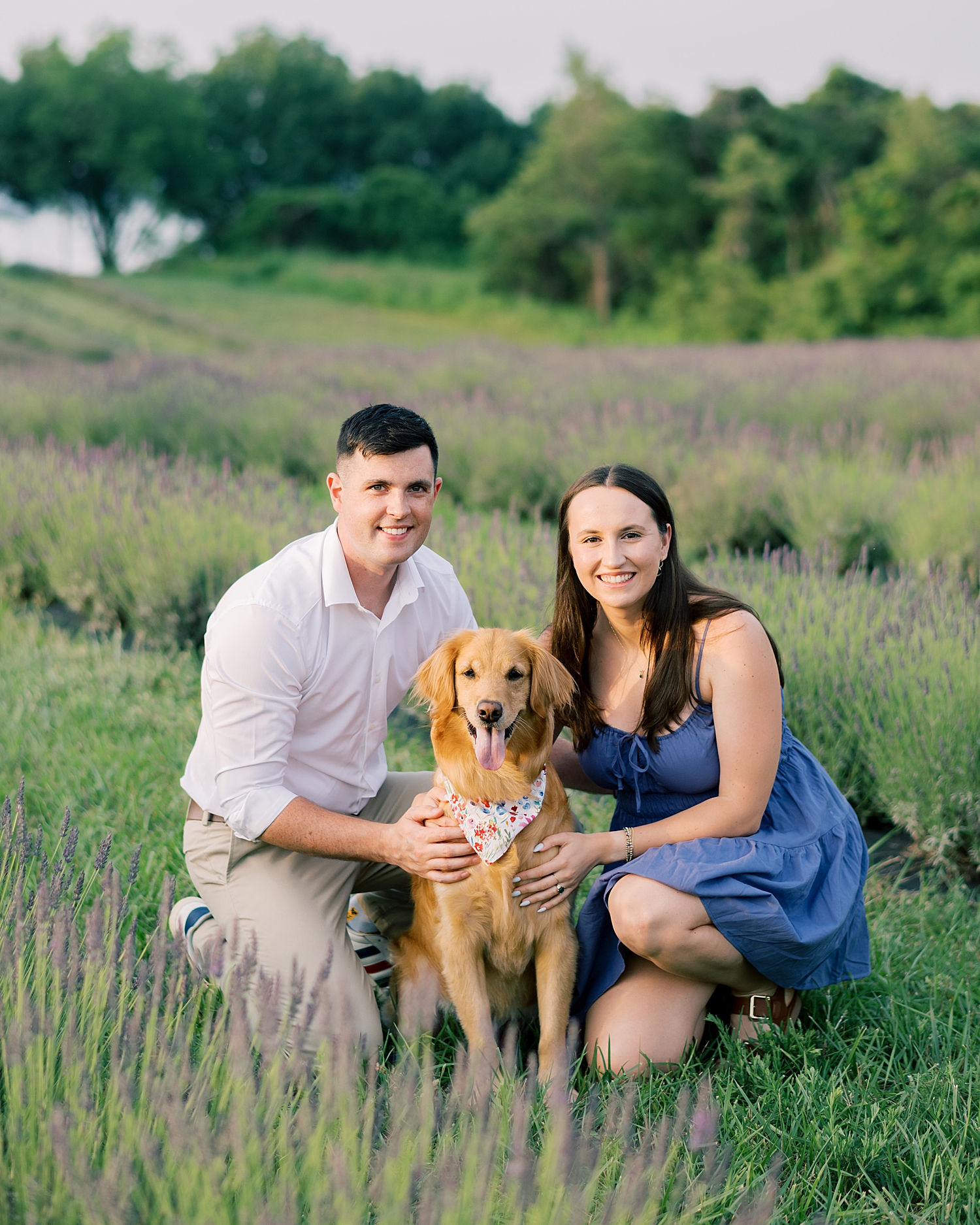 couple kneel next to their dog in field 