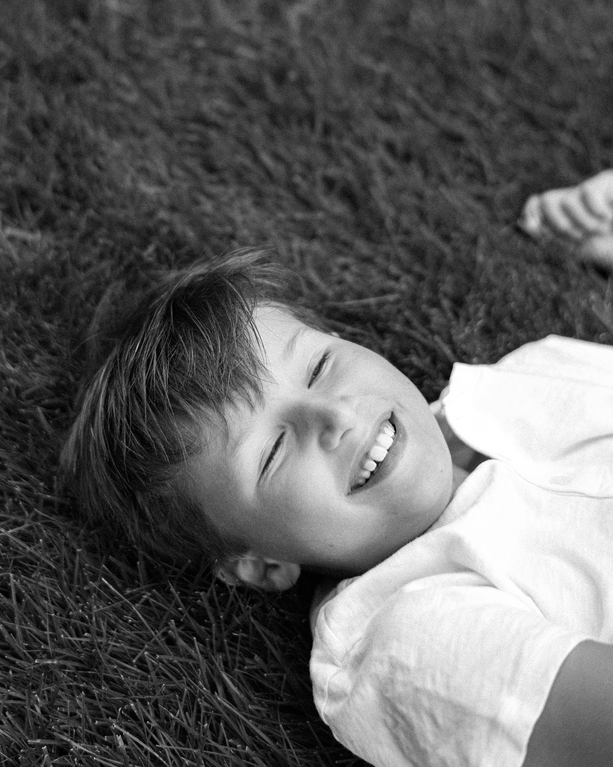 boy rolls around in grass during candid family portraits