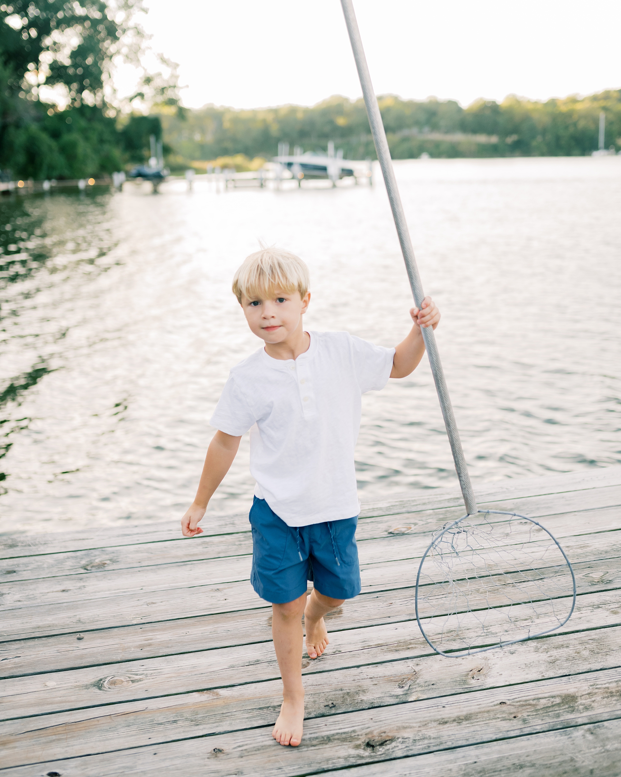 little boy holding net on pier by the water