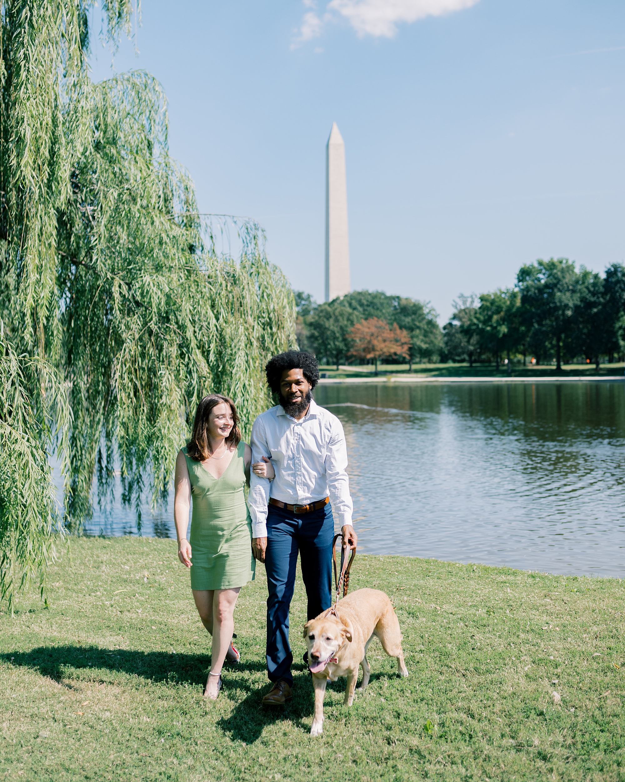 couple walk together with the dog at Constitution Gardens with Washington Monument in the background 