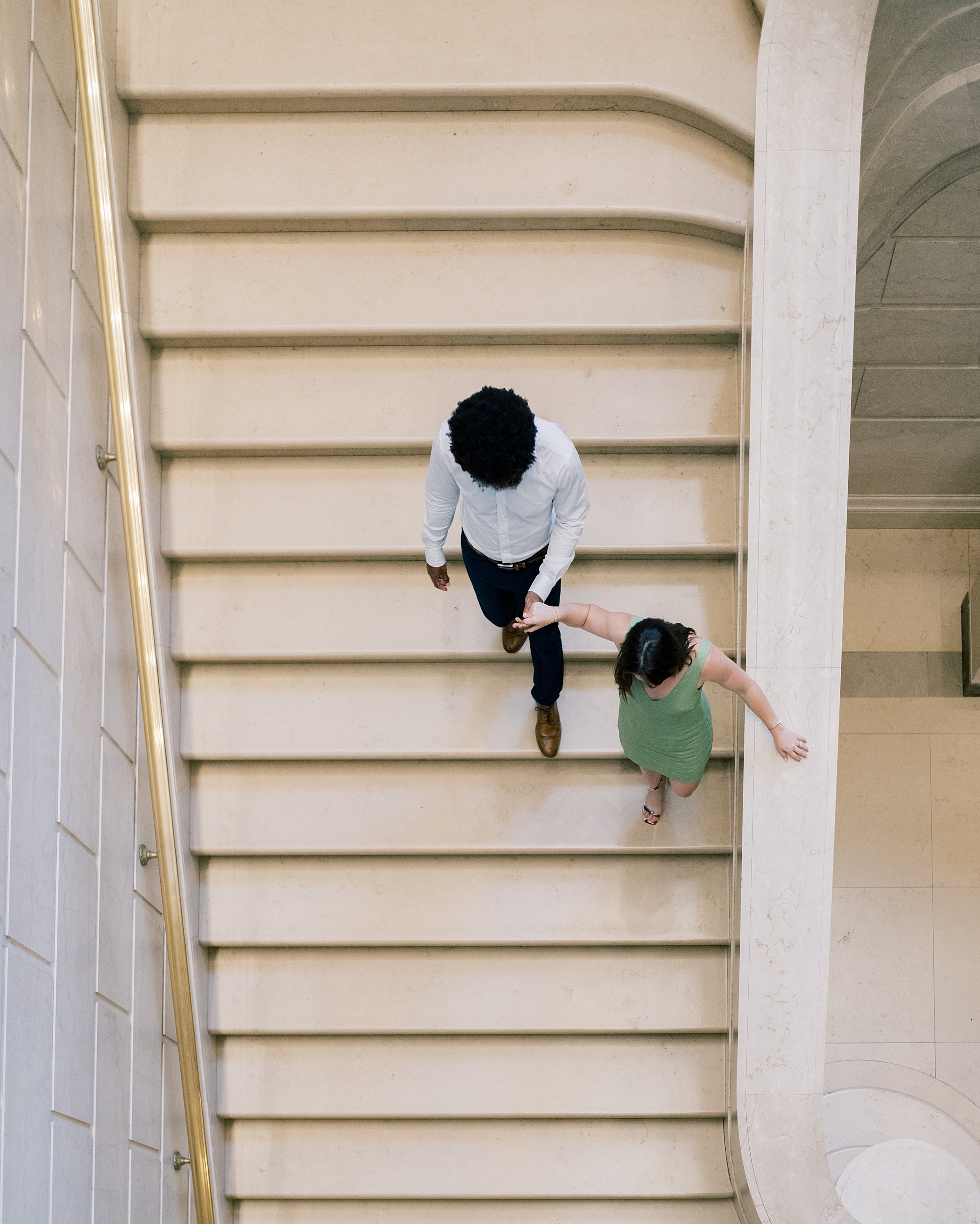 couple hold hands as they walk down stairs at art museum 