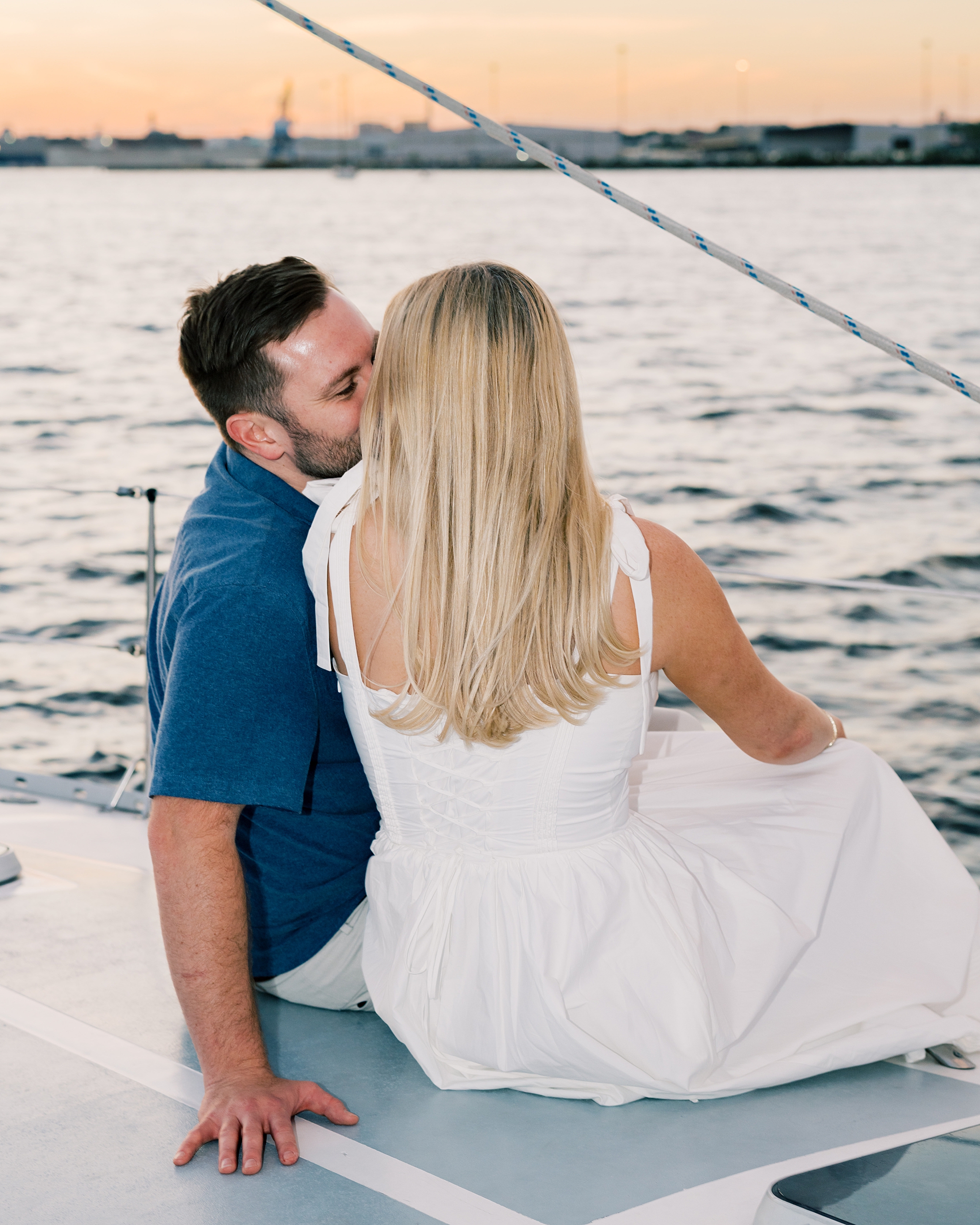 couple kiss while sitting on sailboat watching the sunset 