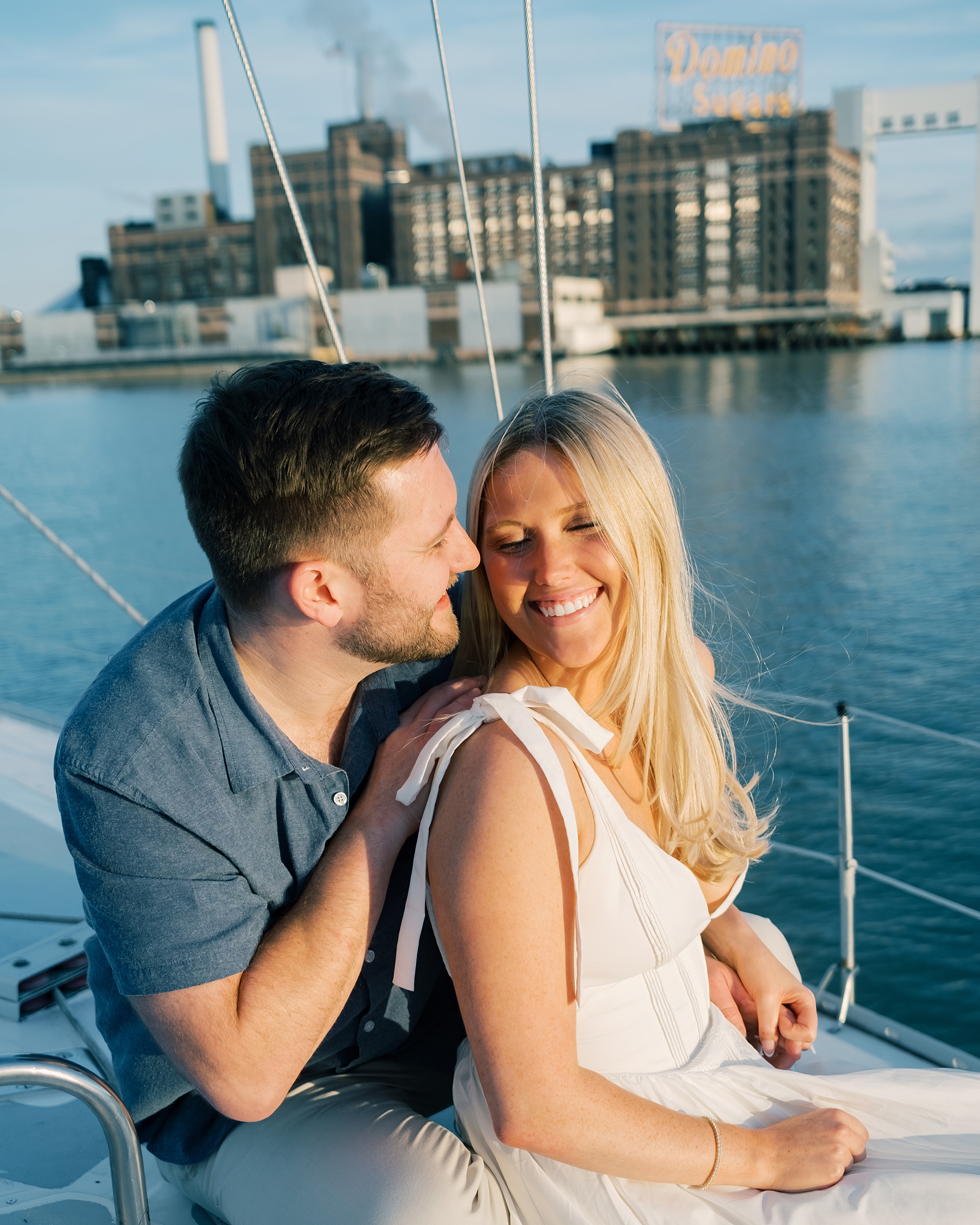 engaged couple sit together on sailboat with Baltimore skyline in the background 