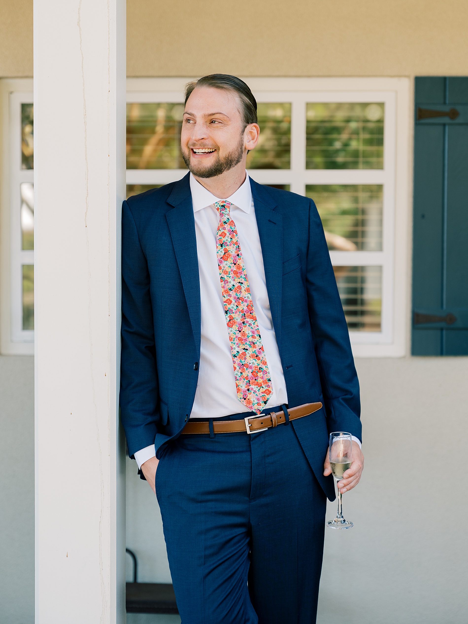 groom leans against porch post in suit