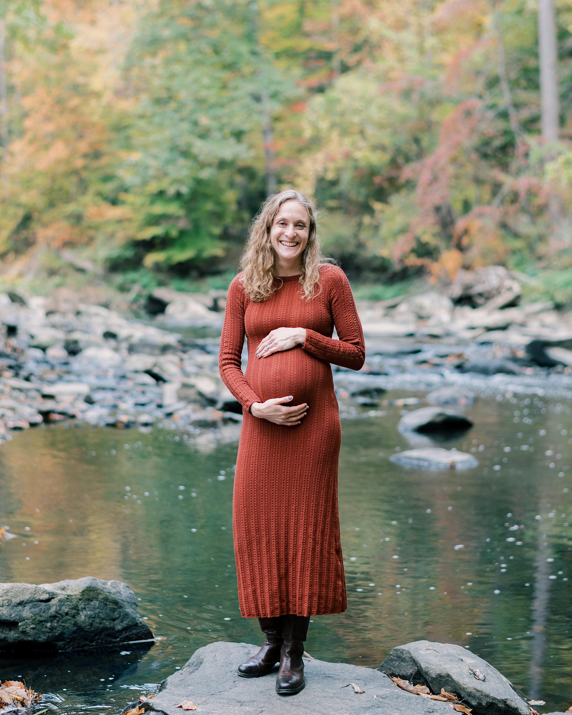 woman stands by water holding baby bump