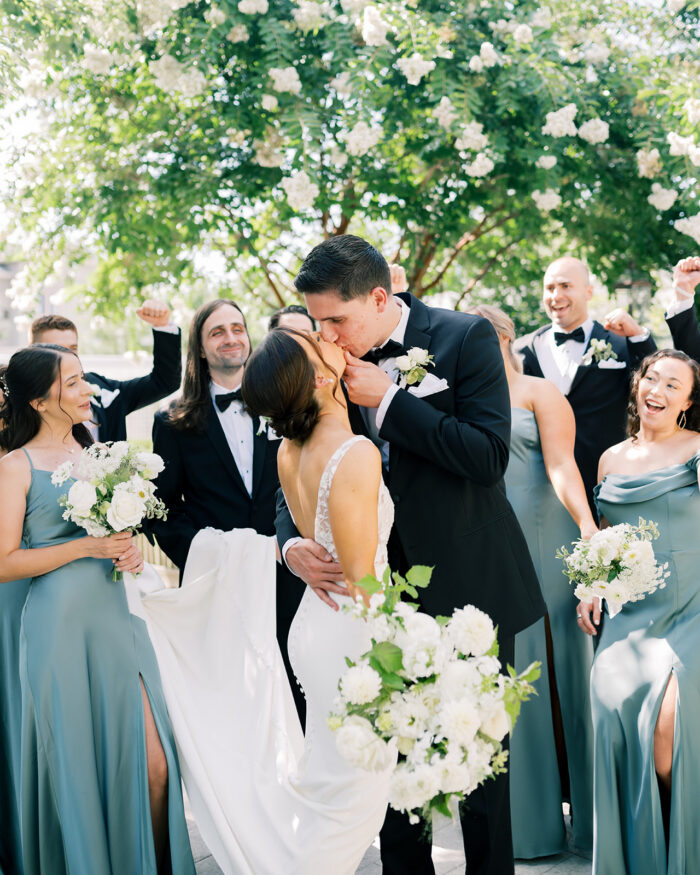 The bride and groom share a kiss surrounded by the bridal party 