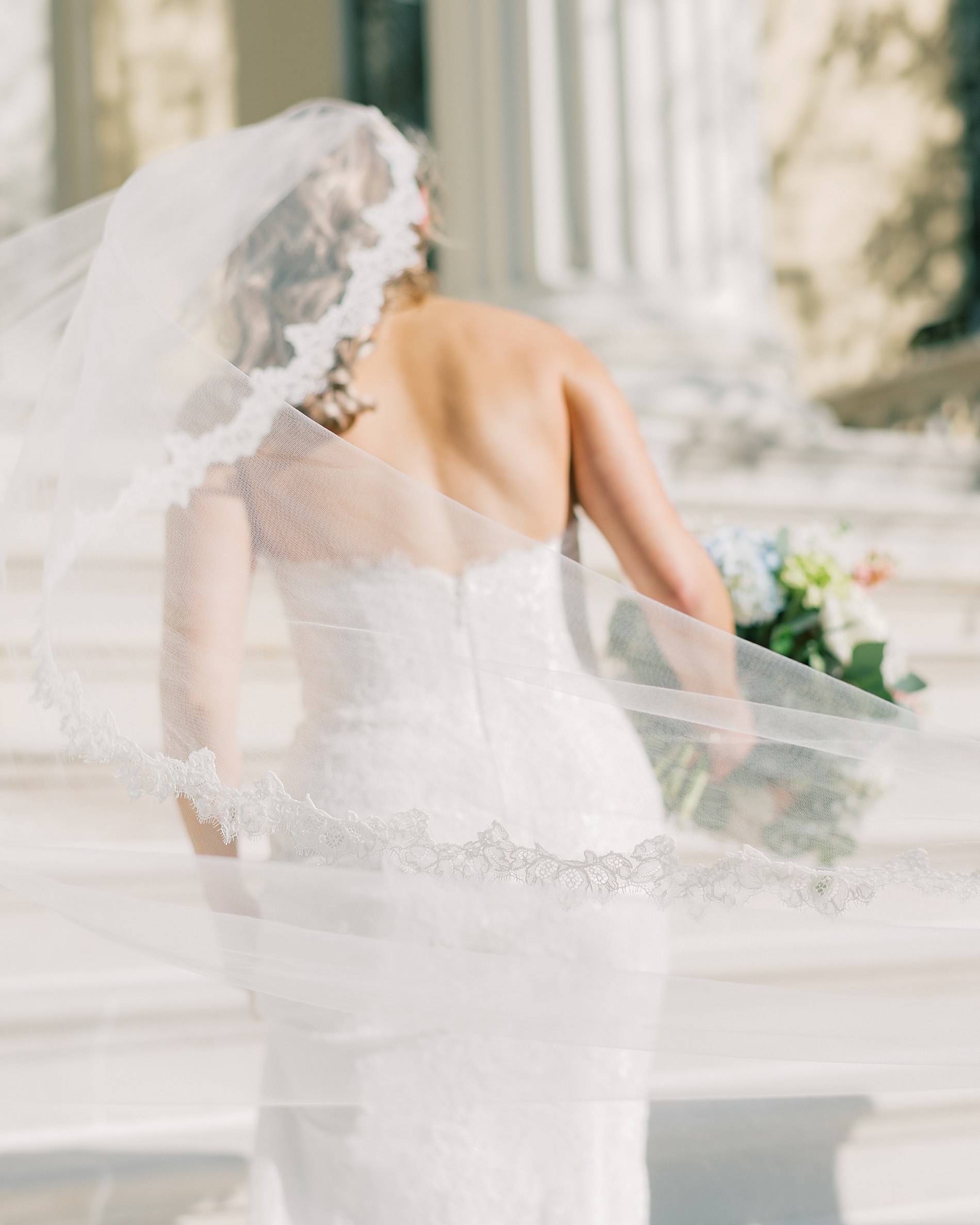 bride walks up stairs of Evergreen library with veil flowing behind her 