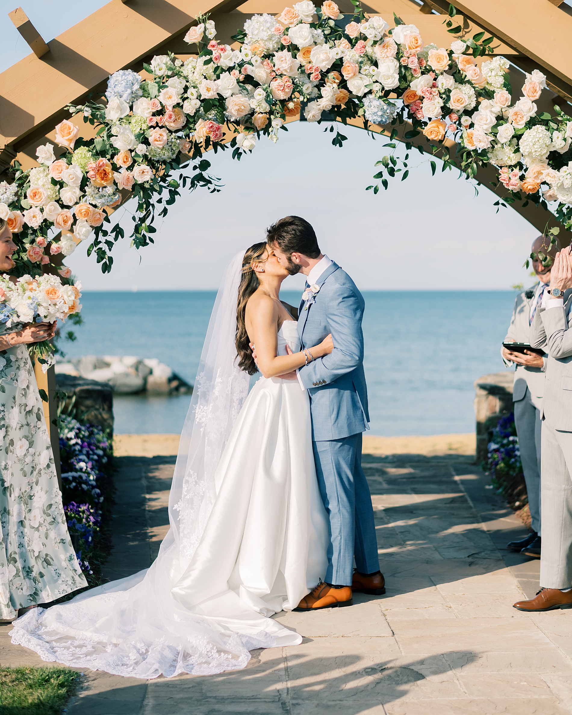 bride and groom kiss under wooden wedding arch decorated with flowers 