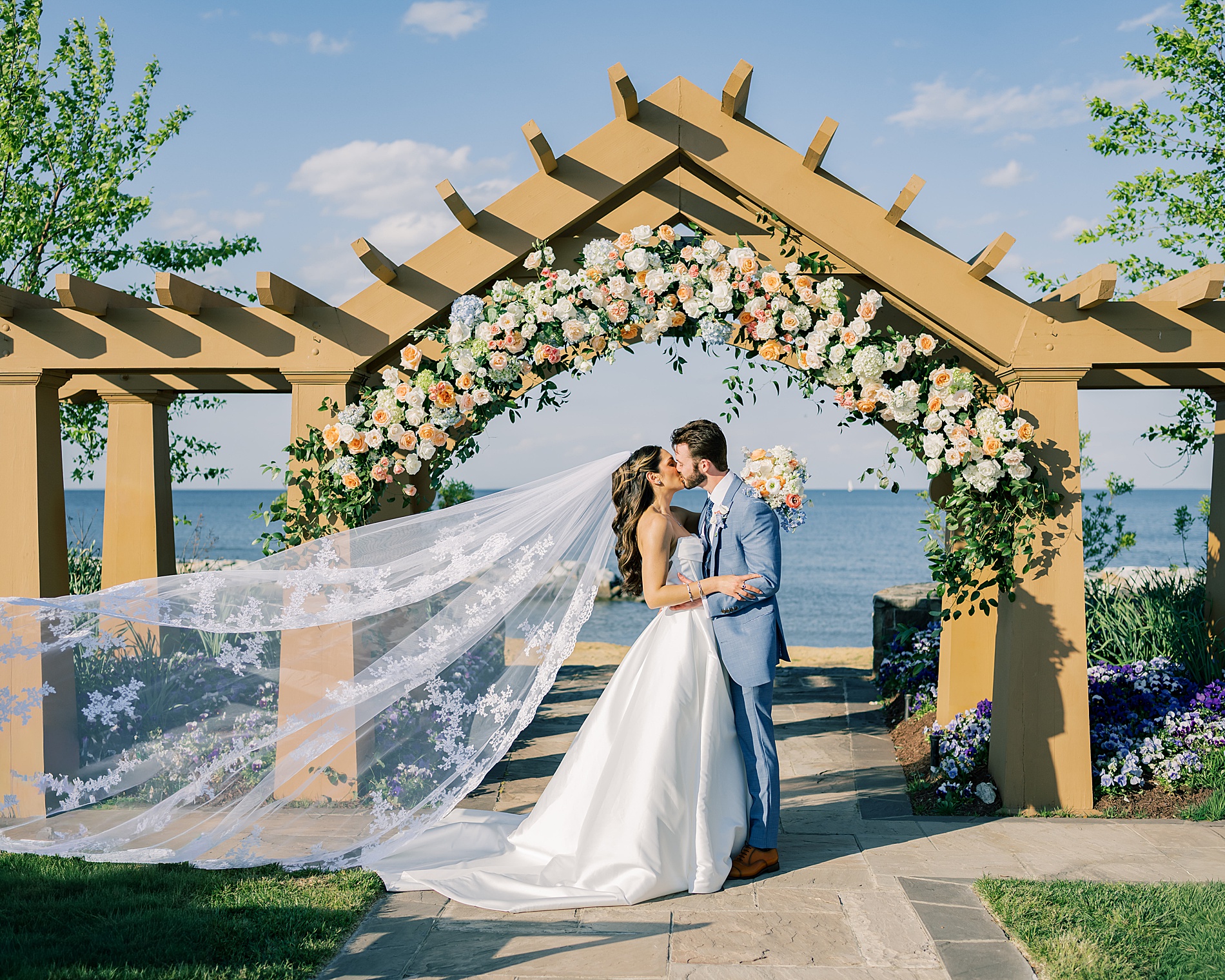 romantic wedding portraits of newlyweds under wedding arch by Chesapeake Bay with bride's veil flowing in the wind 