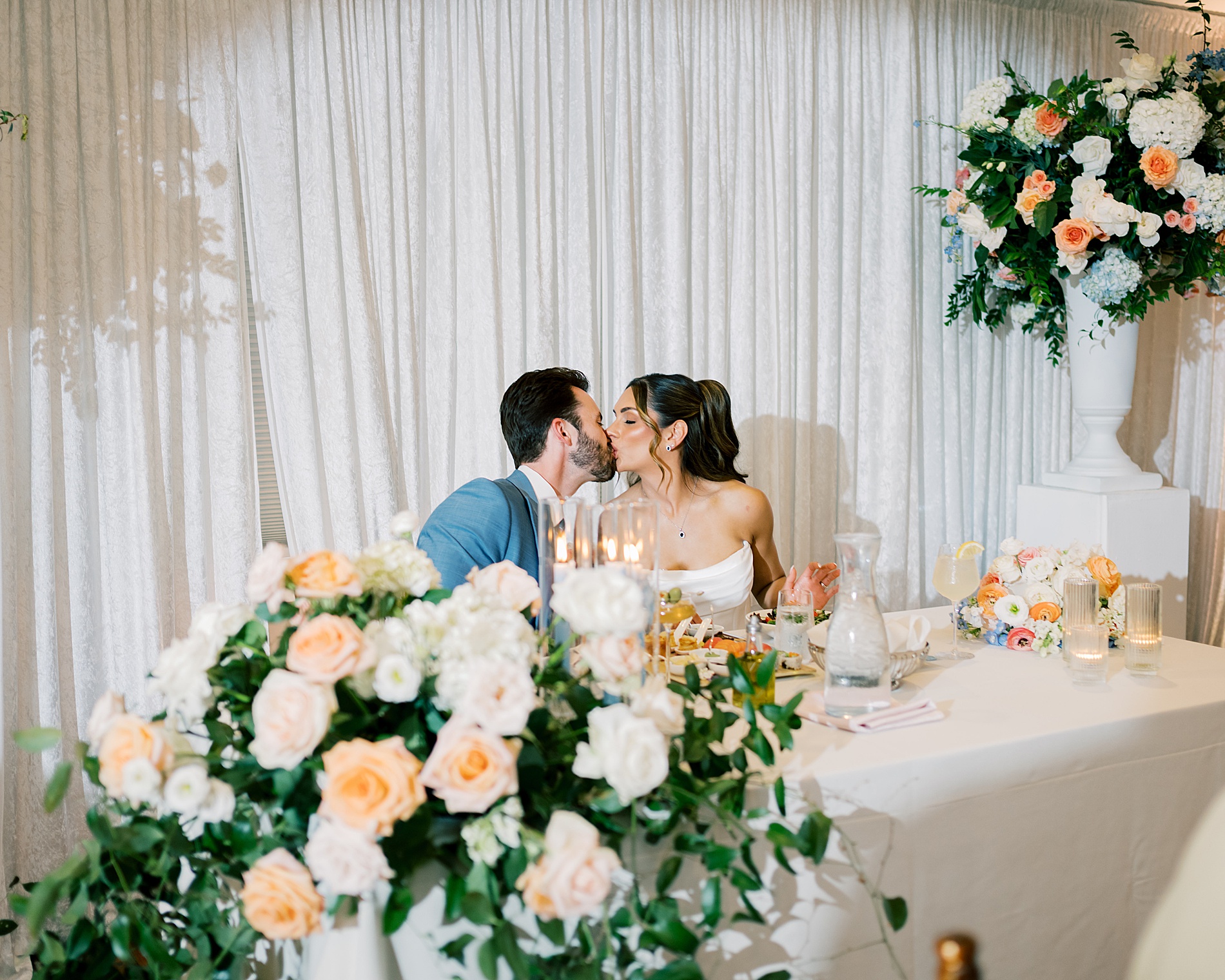 Newlyweds kiss at sweetheart table covered in florals 