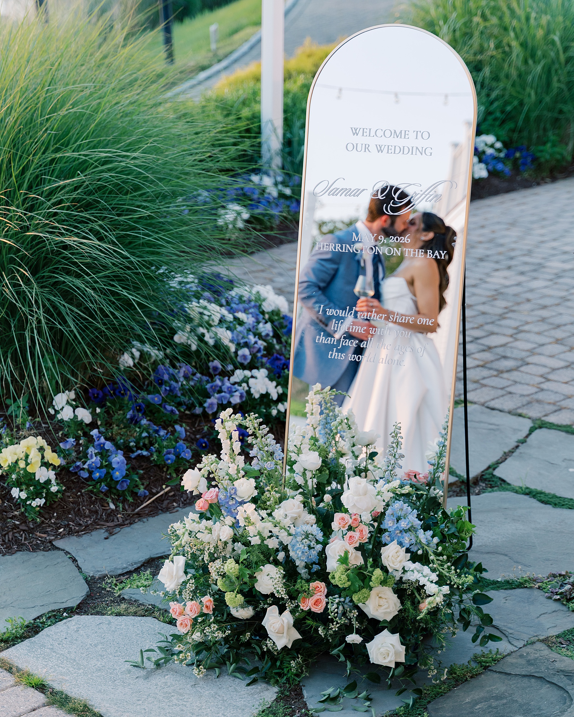 bride and groom kiss and their reflection is seen in the mirrored wedding welcome sign 