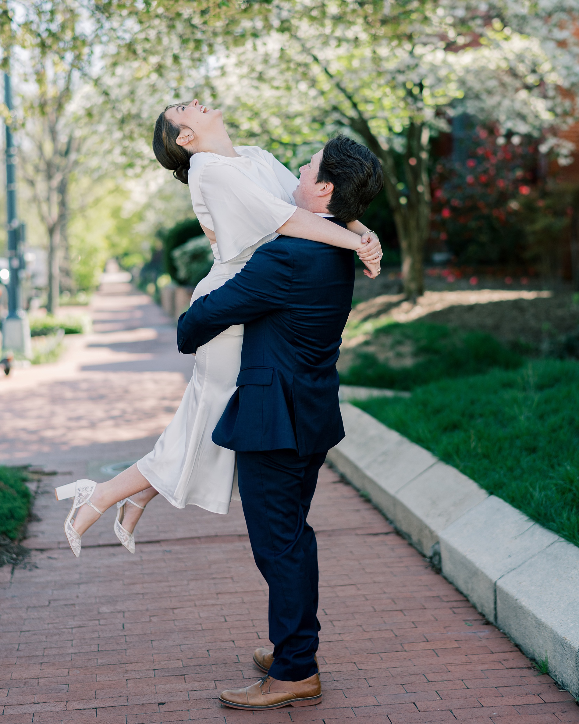 candid engagement photos of couple laughing together as man lifts his fiancé up in his arms 