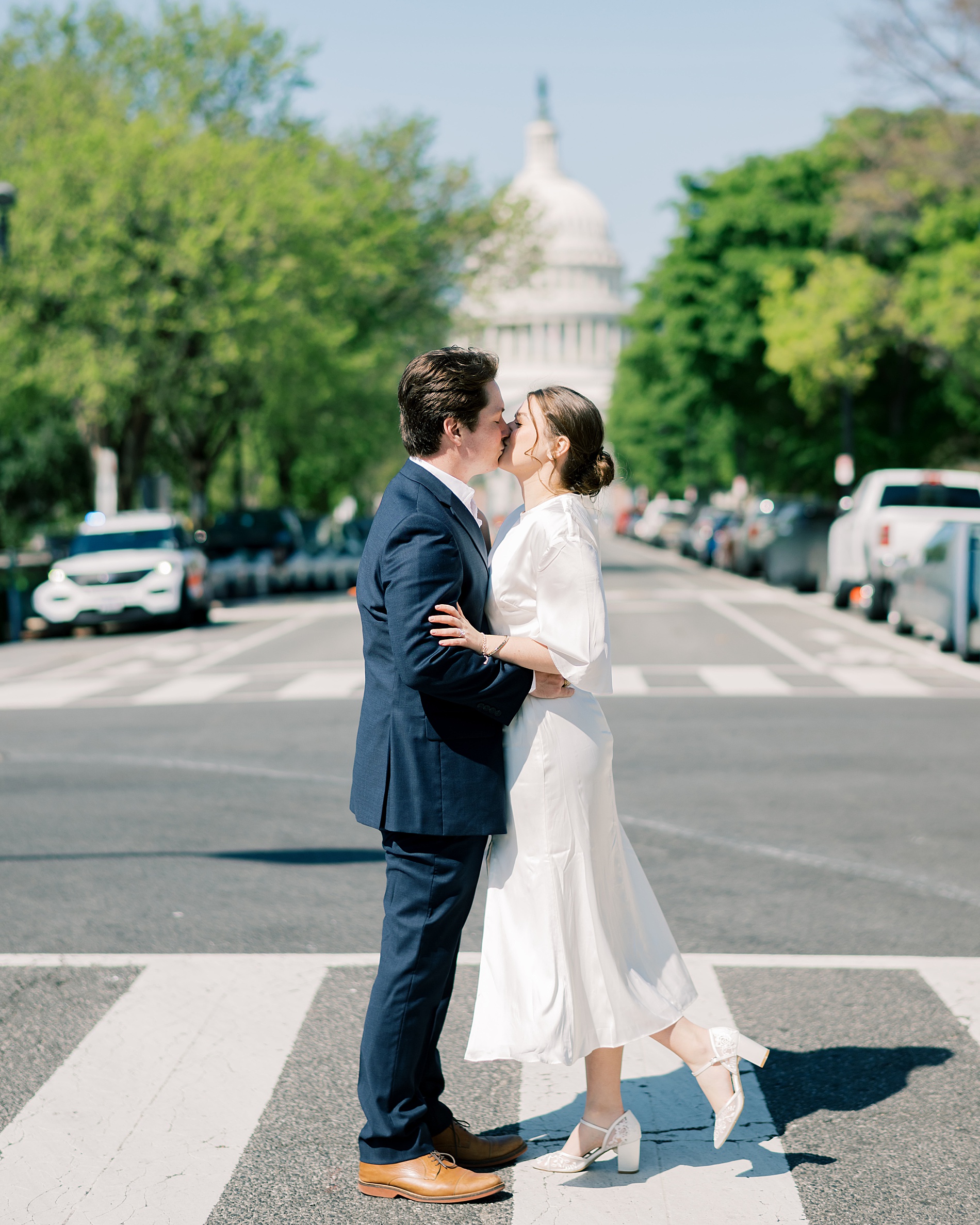 engaged couple kiss in street with Capitol building behind them 