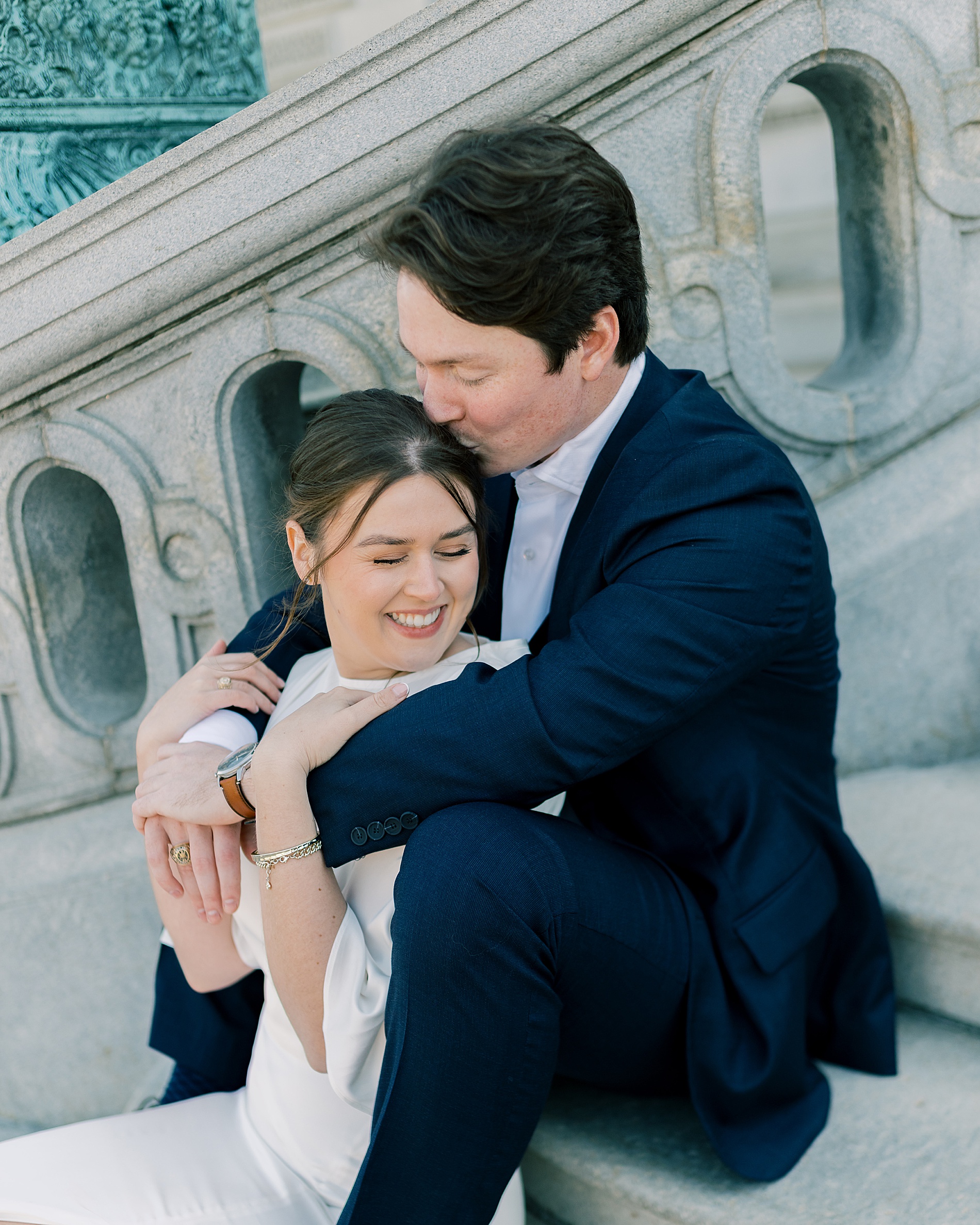 man kisses his fiancé's head as they sit on stairs of Library of Congress